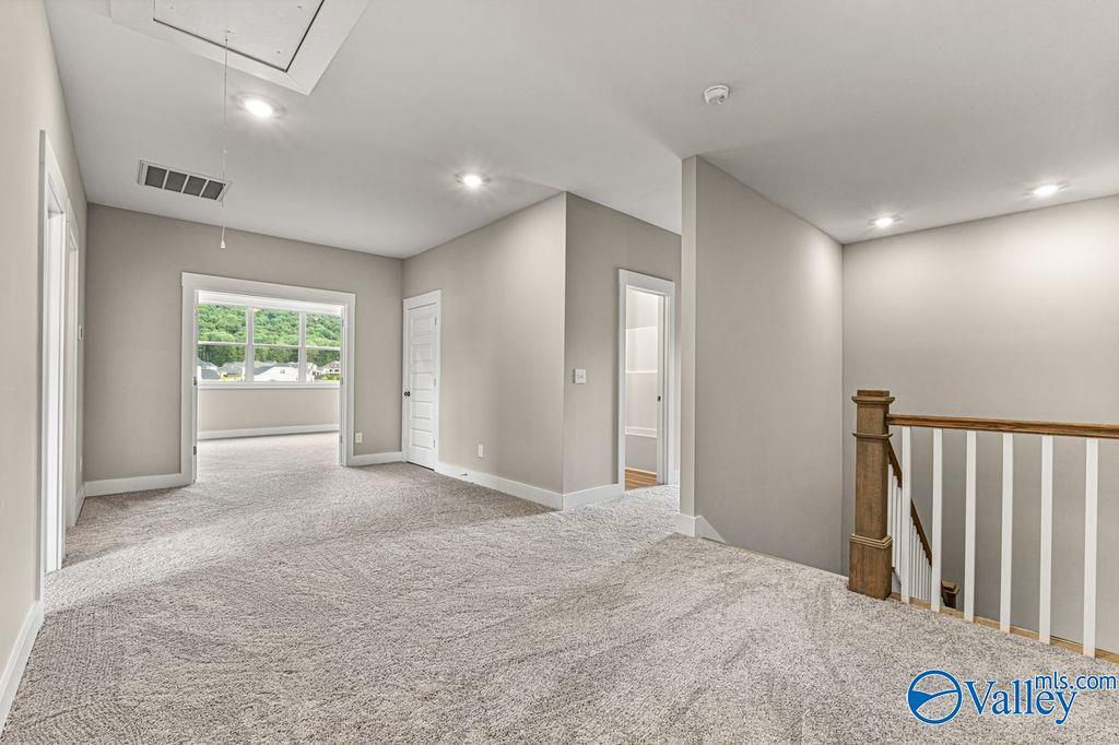 Spacious upstairs hallway with carpeted floors, beige walls, wooden balustrade, and large windows in Evermore Homes The Oxford, Owens Cross Roads, Alabama