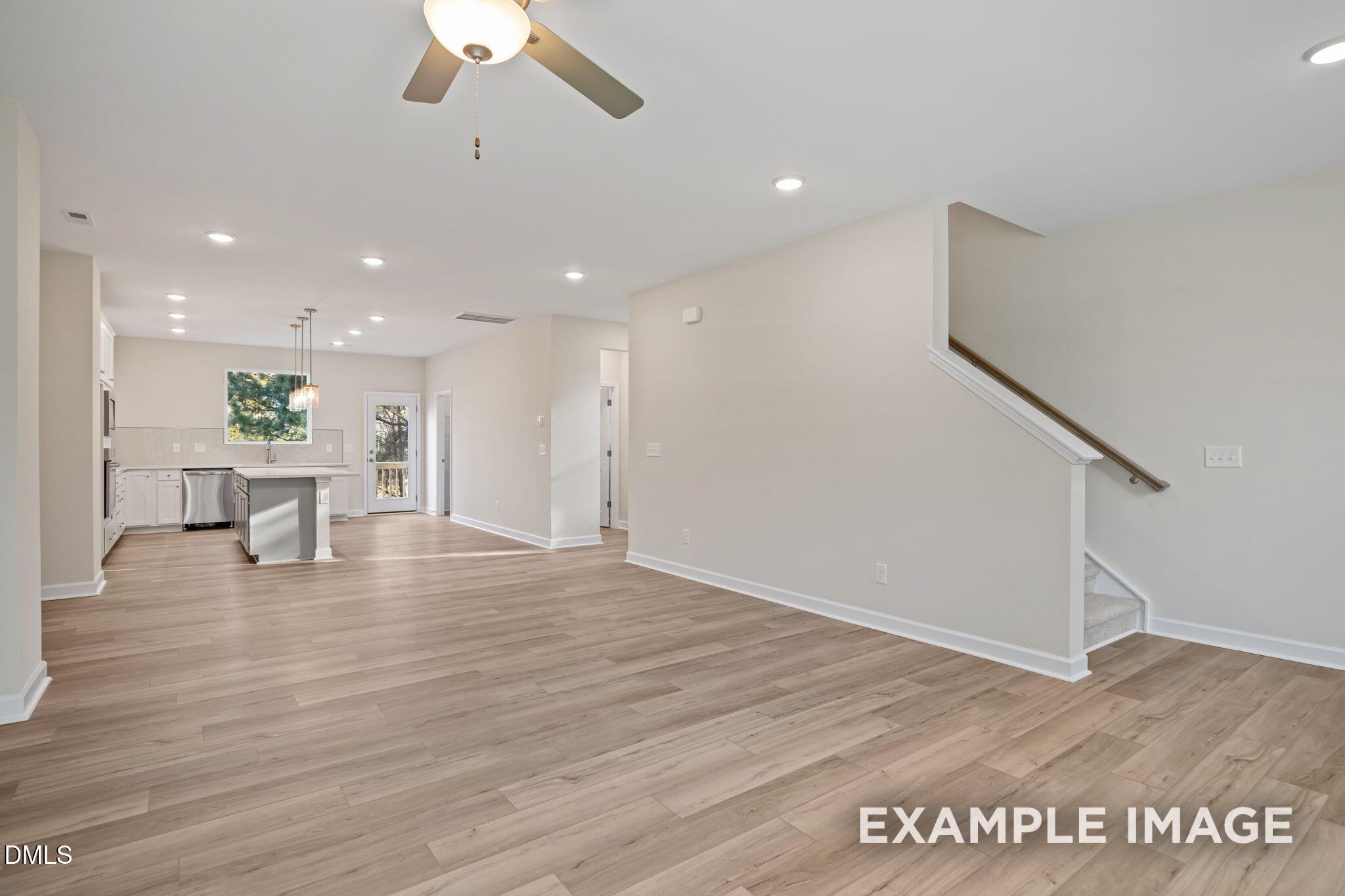 Open-concept kitchen and living area with white cabinets, center island, hardwood floors, and staircase in Davidson Homes The Avery, Knightdale, NC