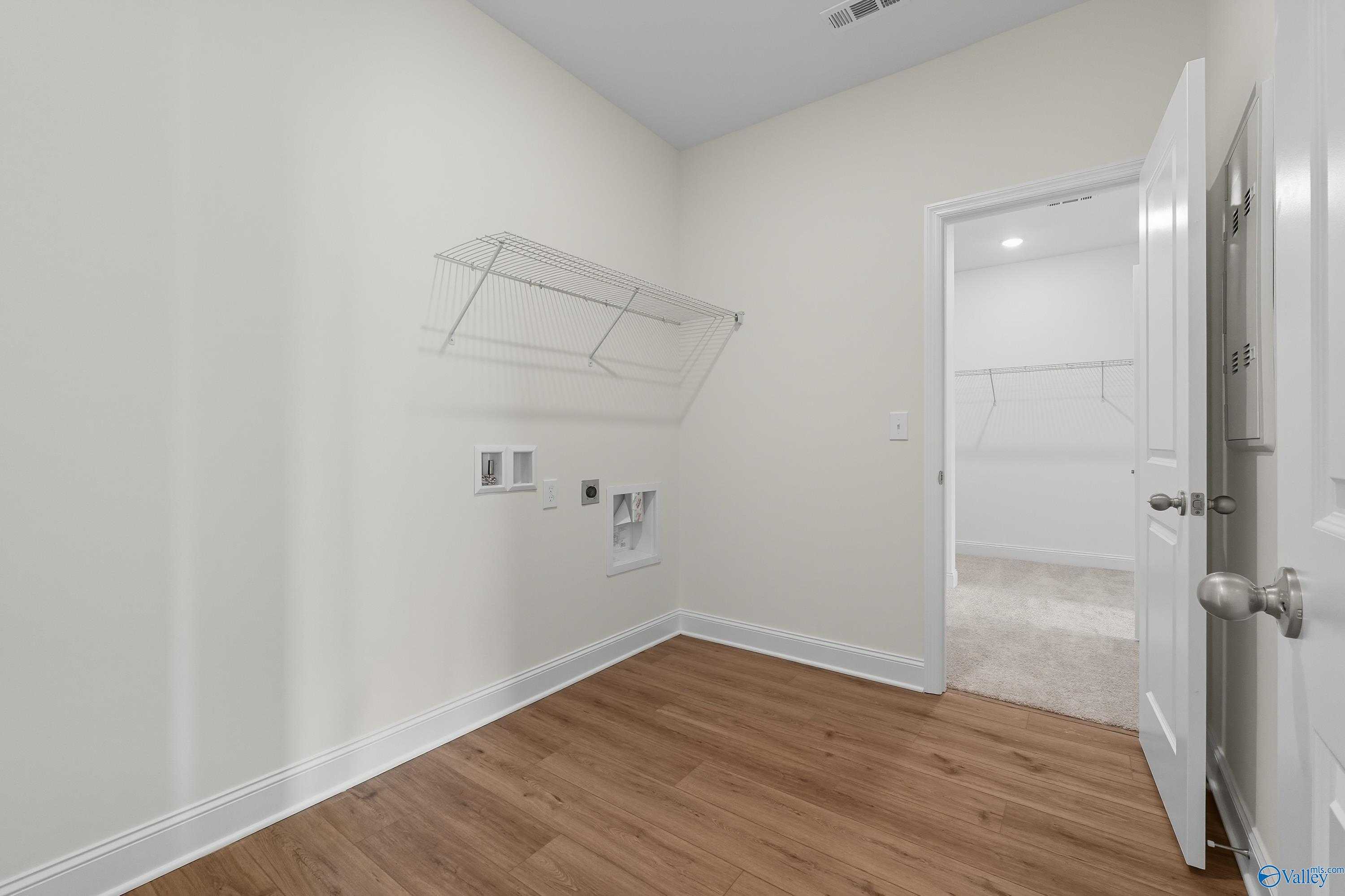 Bright laundry room with open shelving, washer-dryer hookups, and adjacent carpeted bedroom in Davidson Homes The Everett, Meridianville