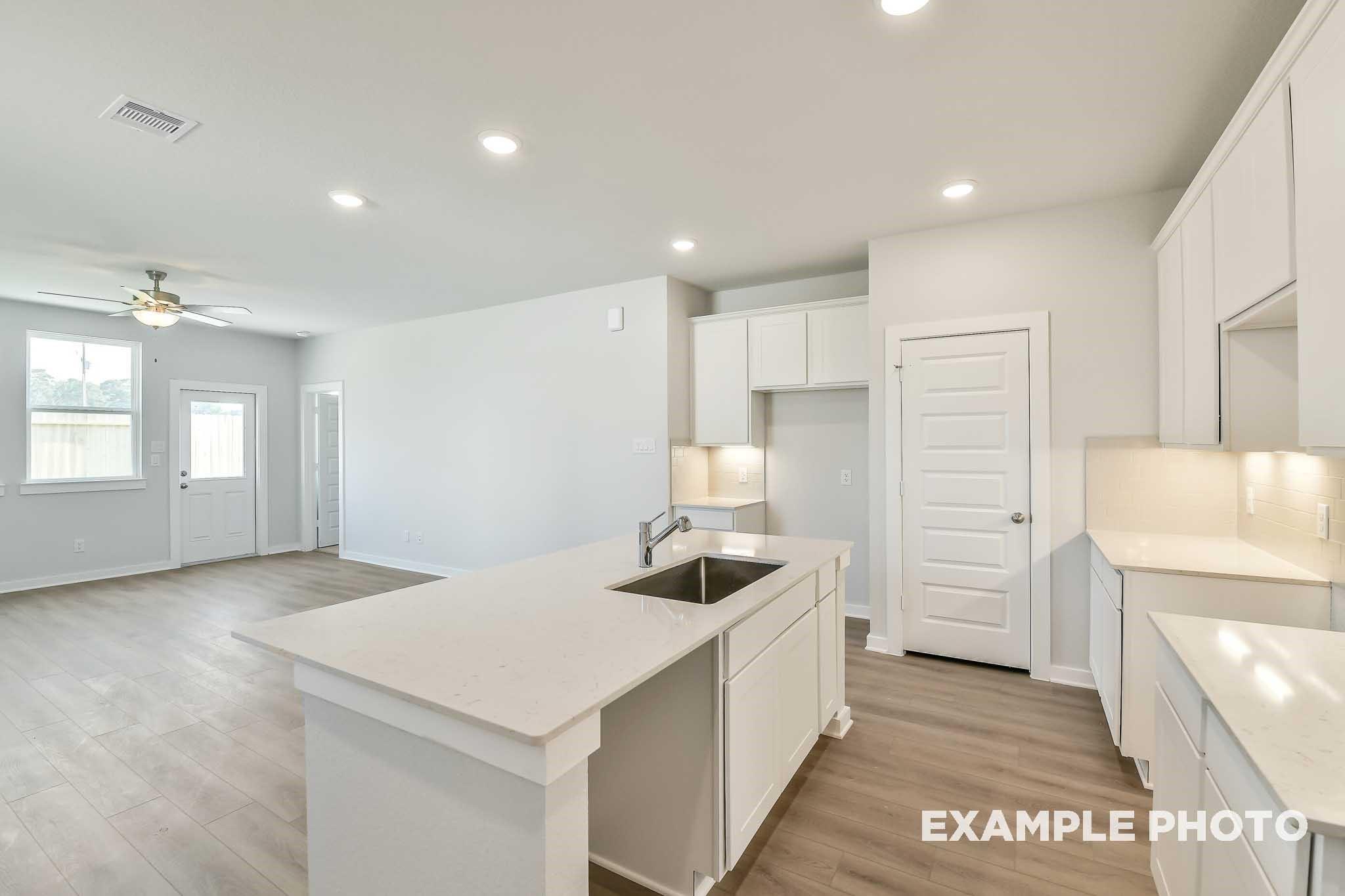 Modern open-concept kitchen with white cabinets, quartz island sink, and ceiling fan in Davidson Homes The Colorado G, Conroe, Texas