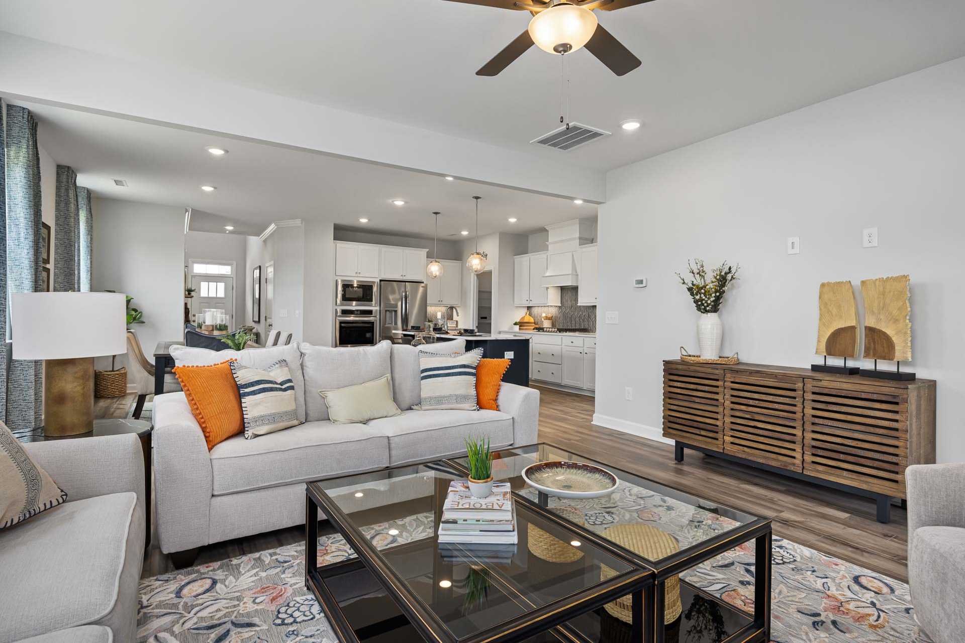 Spacious open-concept living room and kitchen in Beverly Place, Four Oaks, NC by Davidson Homes with white cabinetry, beige sofa, and glass coffee table