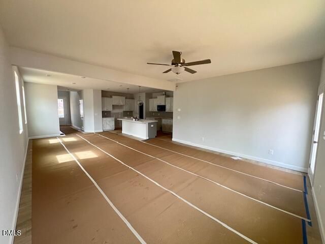 Open-concept kitchen-living area with white cabinetry, central island, ceiling fan, and natural light in Adalynn B home, Lillington, NC