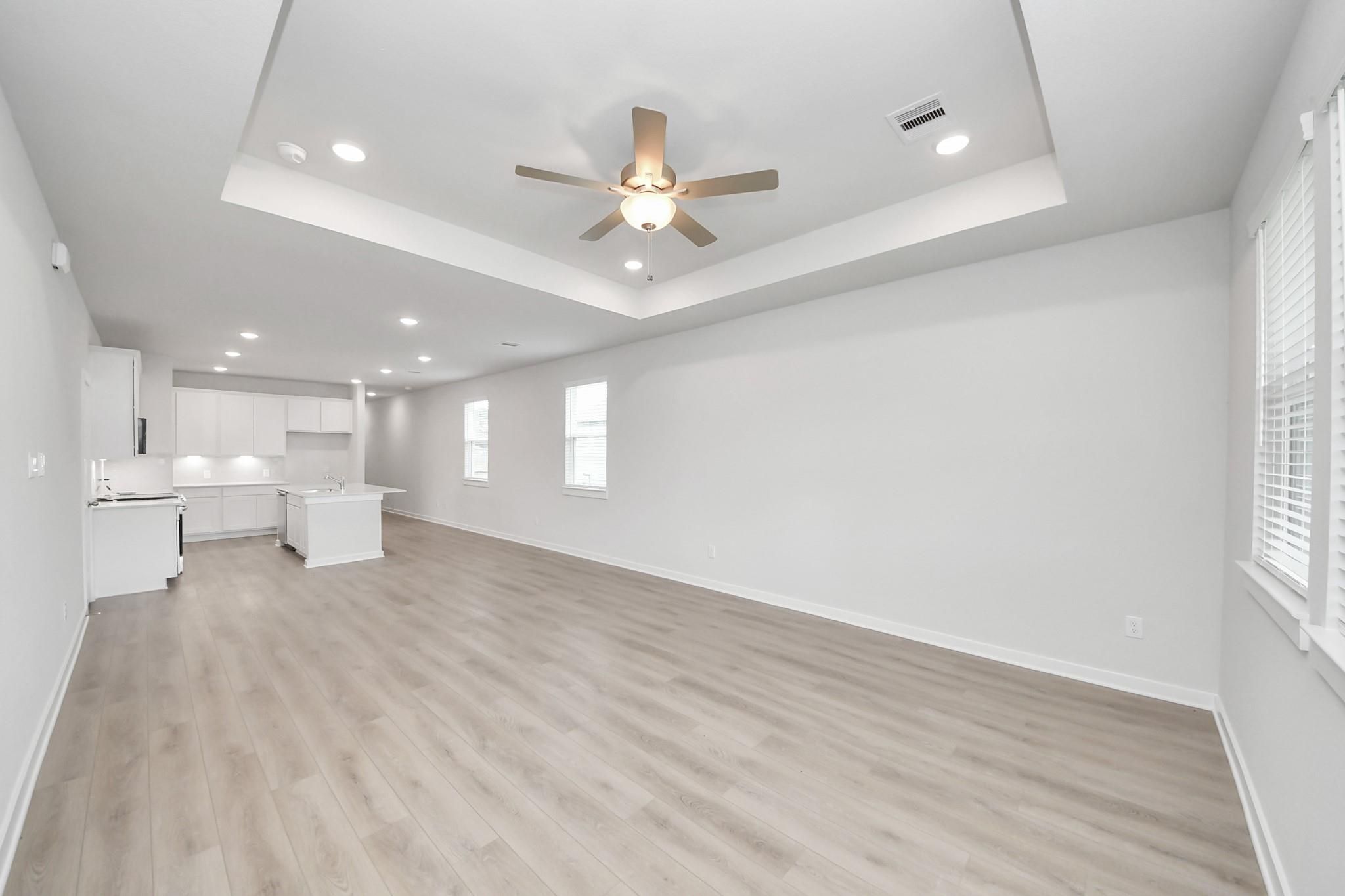 Open-concept living room with tray ceiling and kitchen in The Frio F floor plan at Liberty Estates, Cleveland, Texas.