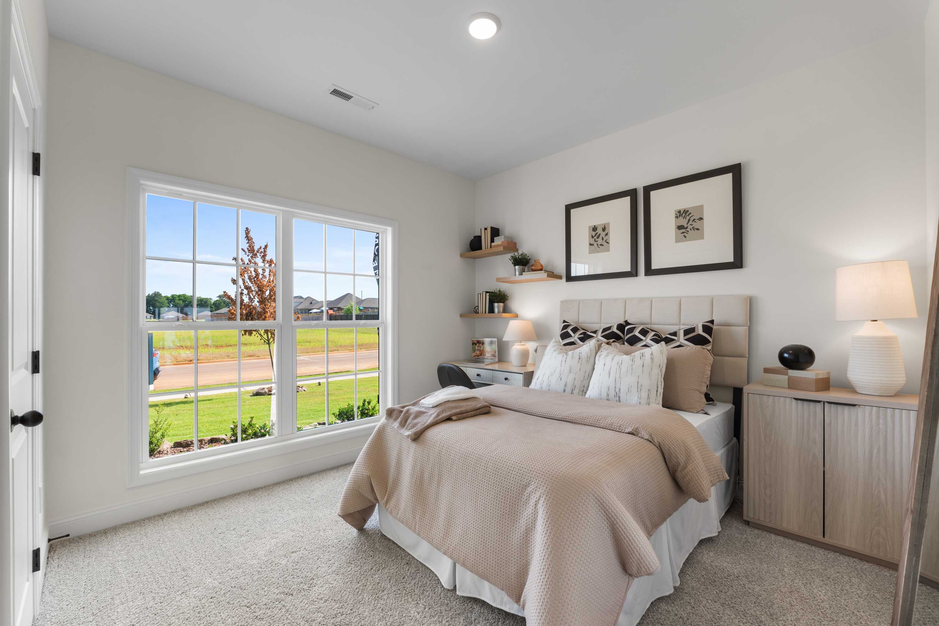 Cozy bedroom at Lynn Meadows in Meridianville AL with beige bed, large window overlooking green fields, bookshelves and lamps