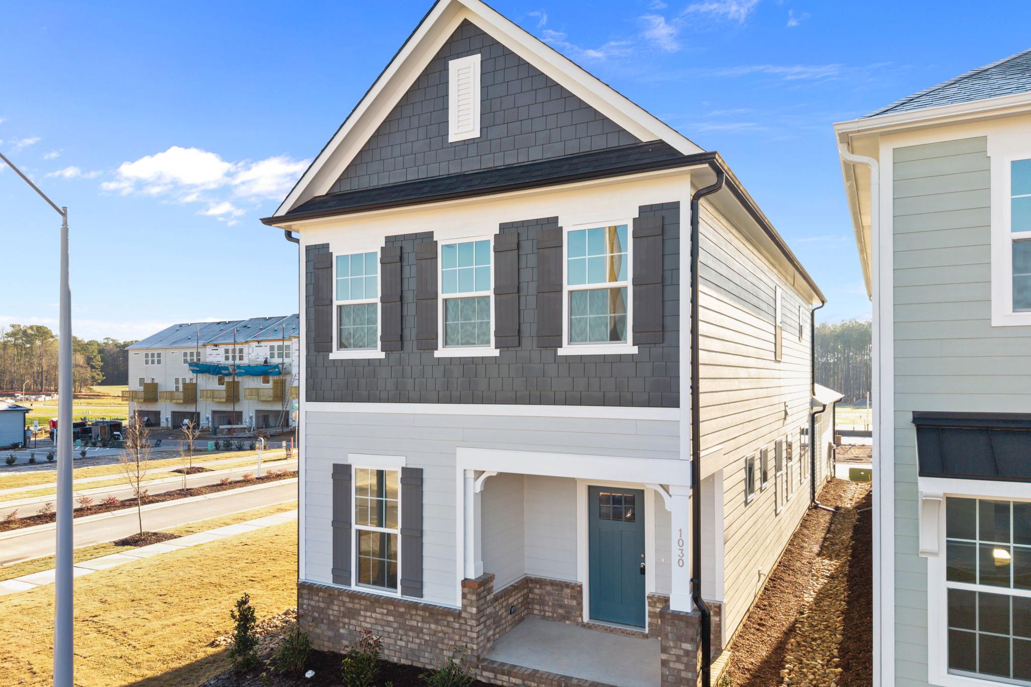 Two-story craftsman home exterior at Forestville Yard in Knightdale NC with gray siding, covered porch, blue door, and brick base