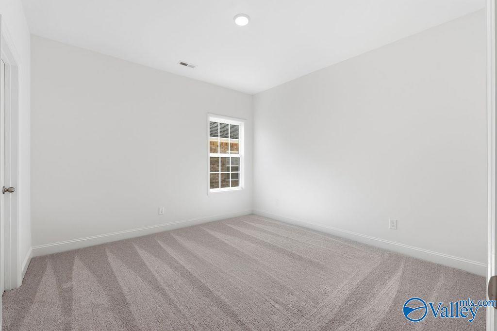 Bright secondary bedroom with white walls, large window, and plush beige carpet in Davidson Homes The Montgomery, Hartselle, AL