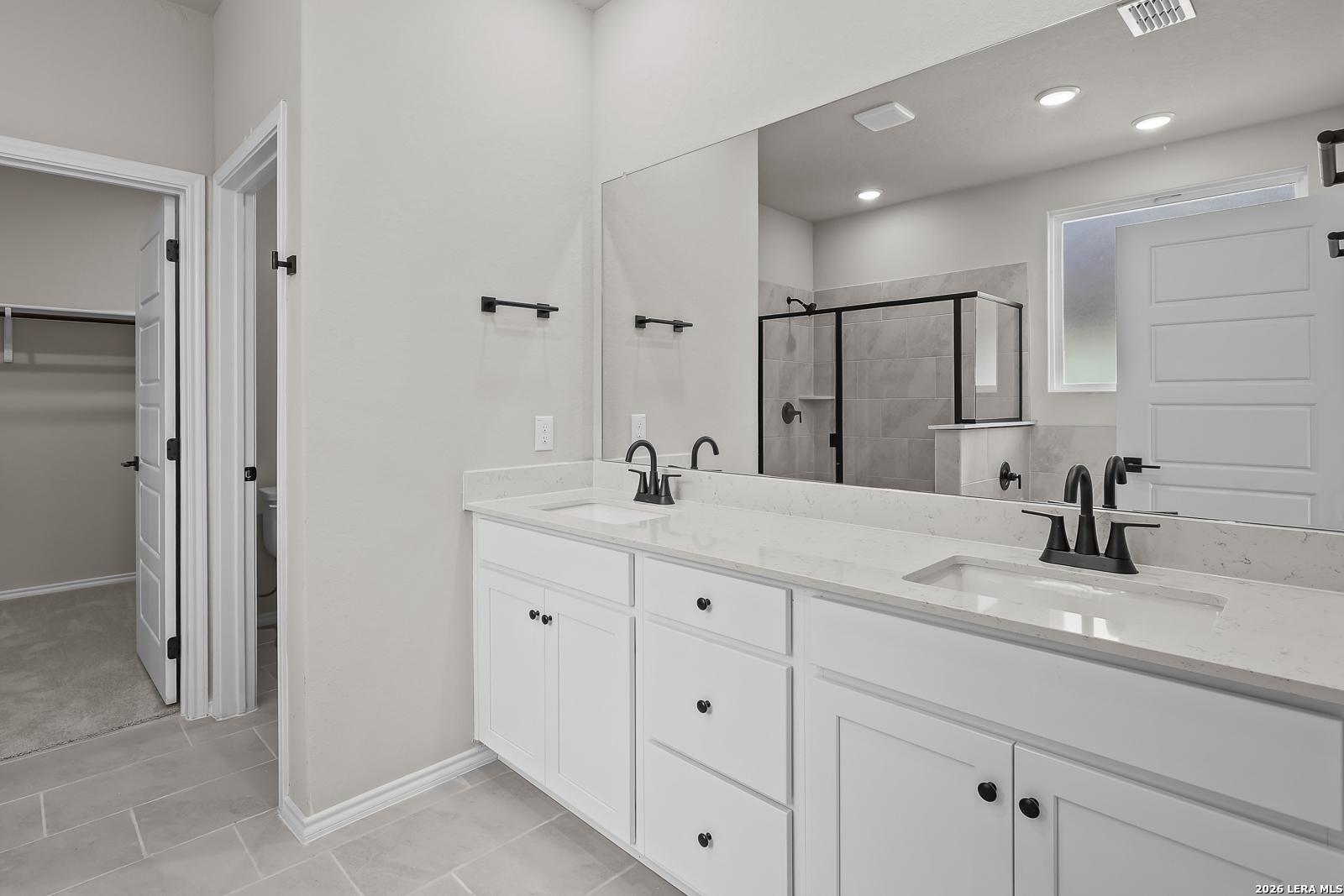 Double vanity bathroom with white cabinets, black fixtures, and tile walk-in shower in Davidson Homes The Sequoia C, San Antonio