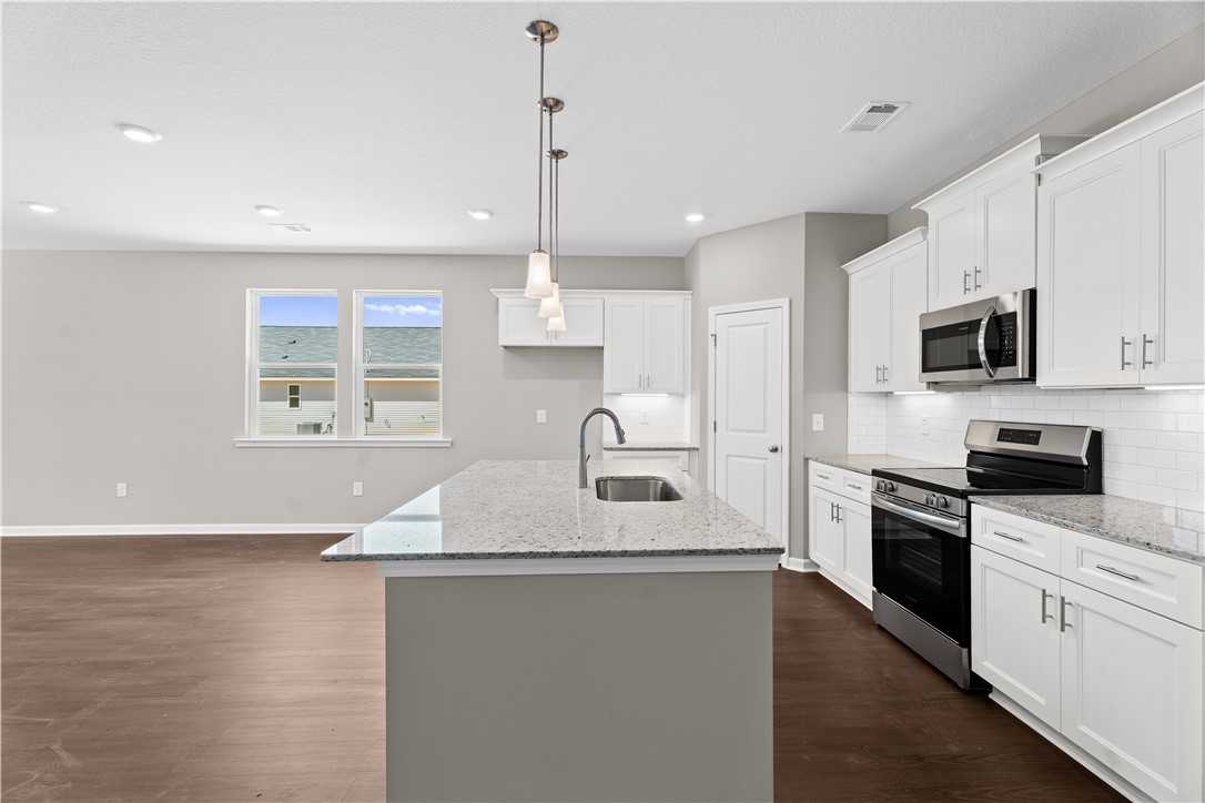 Modern open-concept kitchen with white cabinets, granite island sink, stainless appliances in The Orion 4-bed home, Cusseta, AL
