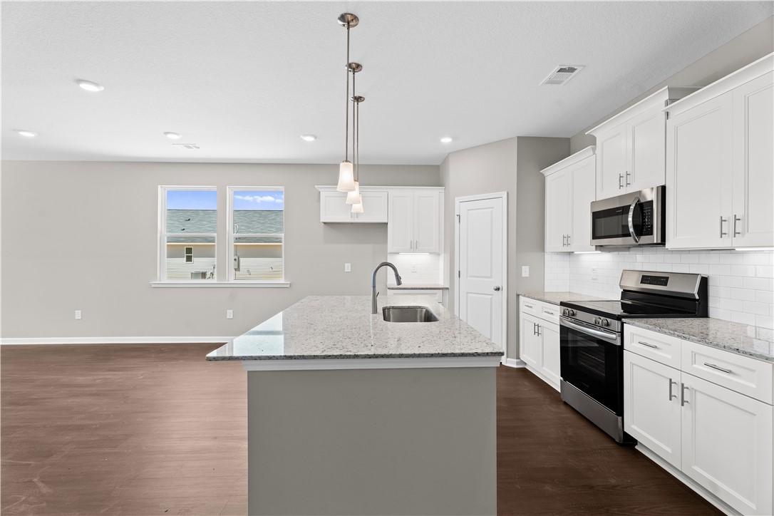 Modern kitchen with white cabinets, granite island sink, stainless appliances in Evermore Homes The Orion, Cusseta, Alabama
