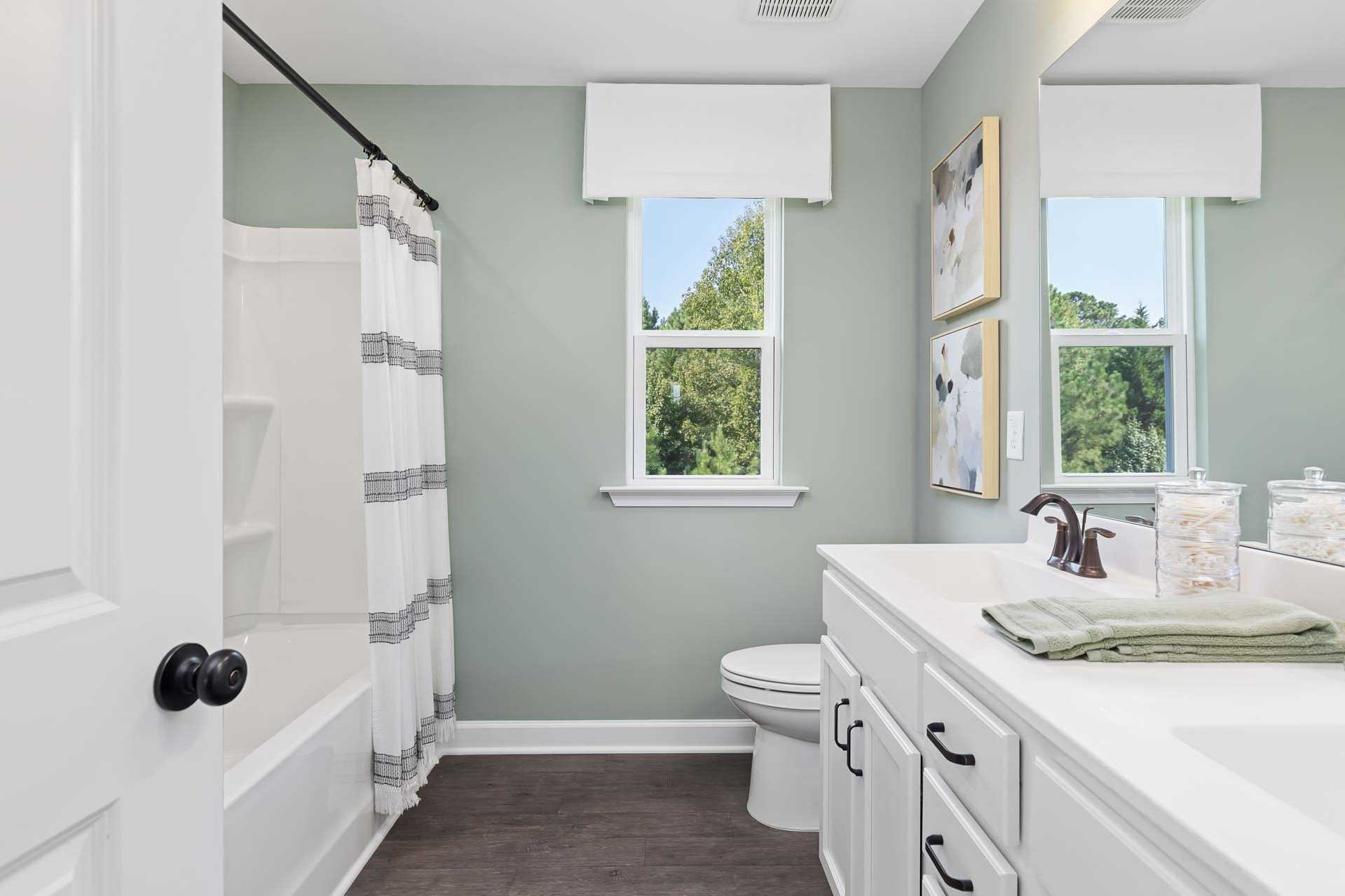 Bright bathroom at Sierra Heights in Clayton NC with sage green walls, white vanity, striped shower curtain, and soaking tub
