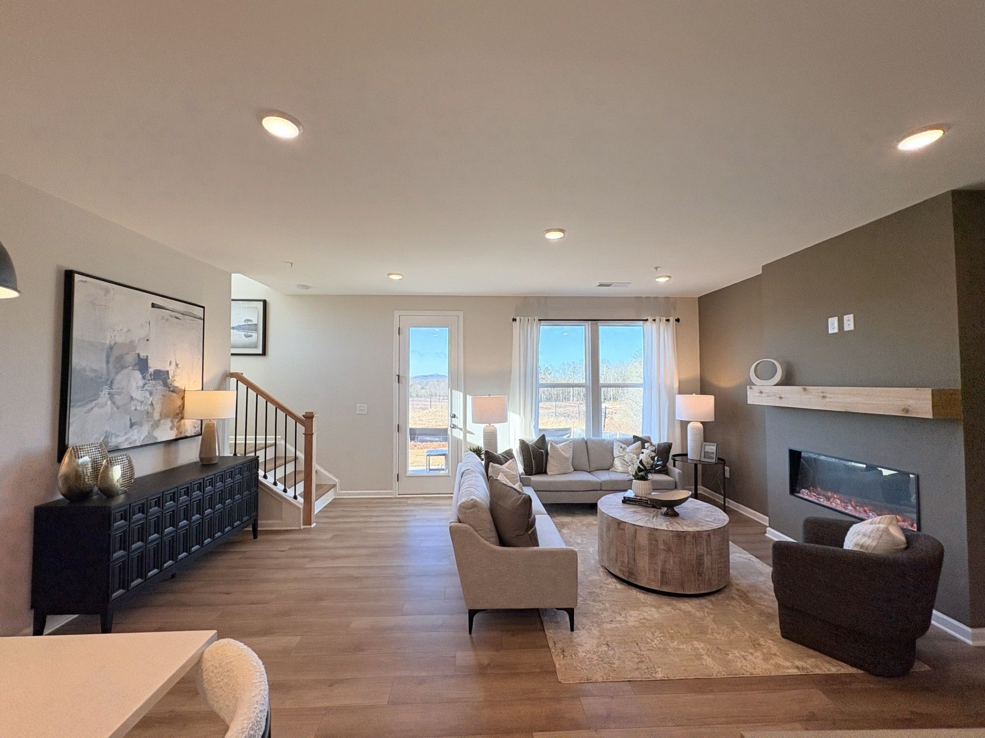 Open-concept living room in Hemingway Cumming GA by Davidson Homes with hardwood floors, modern gas fireplace, and plush sectional sofa
