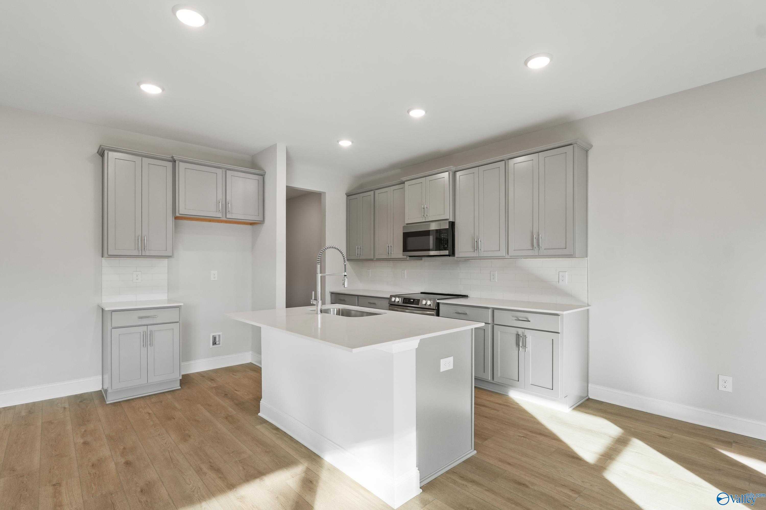 Modern kitchen with gray shaker cabinets, white quartz island, stainless range and sink in The Camden B by Davidson Homes, Huntsville AL