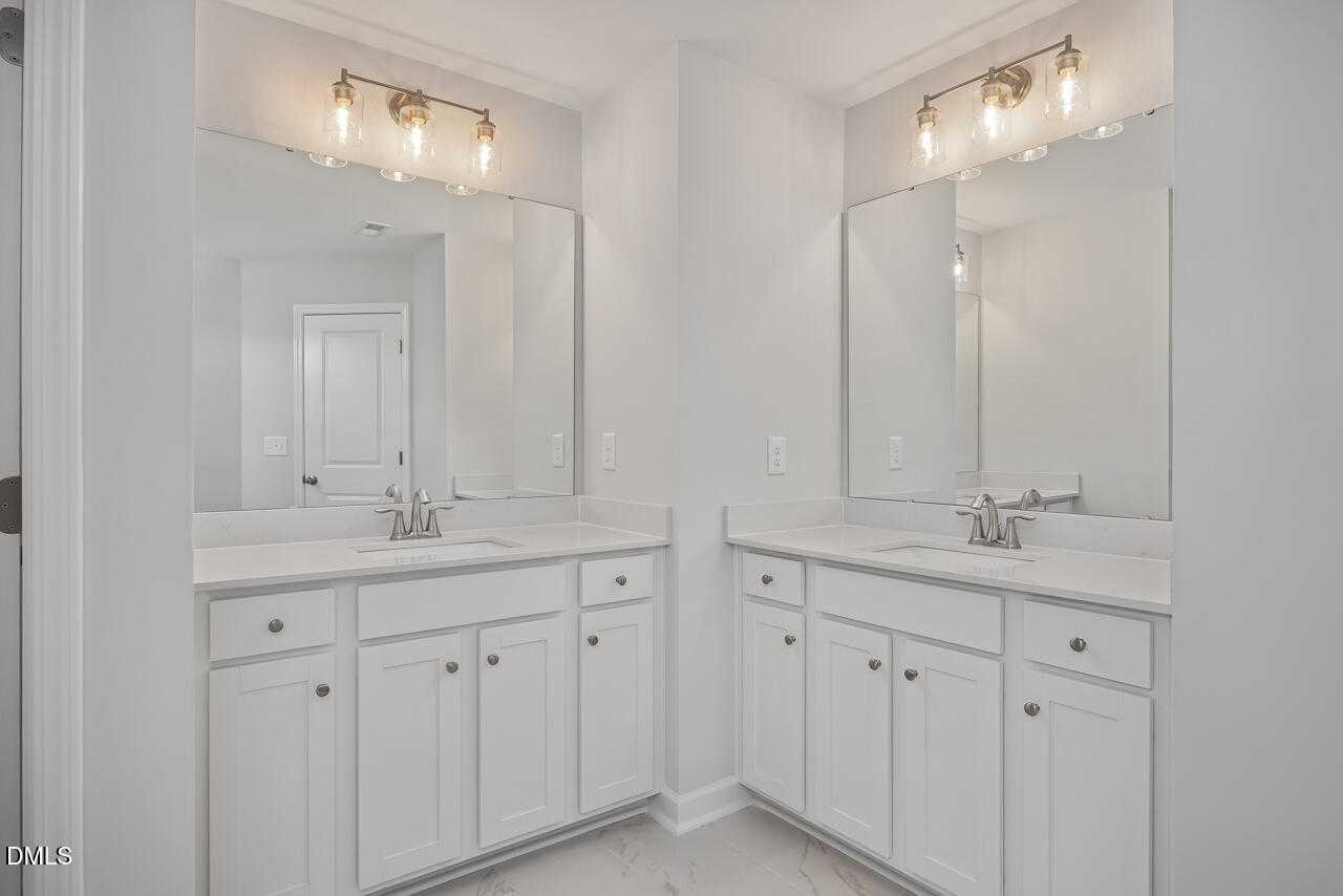 Modern double vanity bathroom with white cabinets, undermount sinks, and sconce lighting in Davidson Homes The Graham, Fuquay-Varina, NC