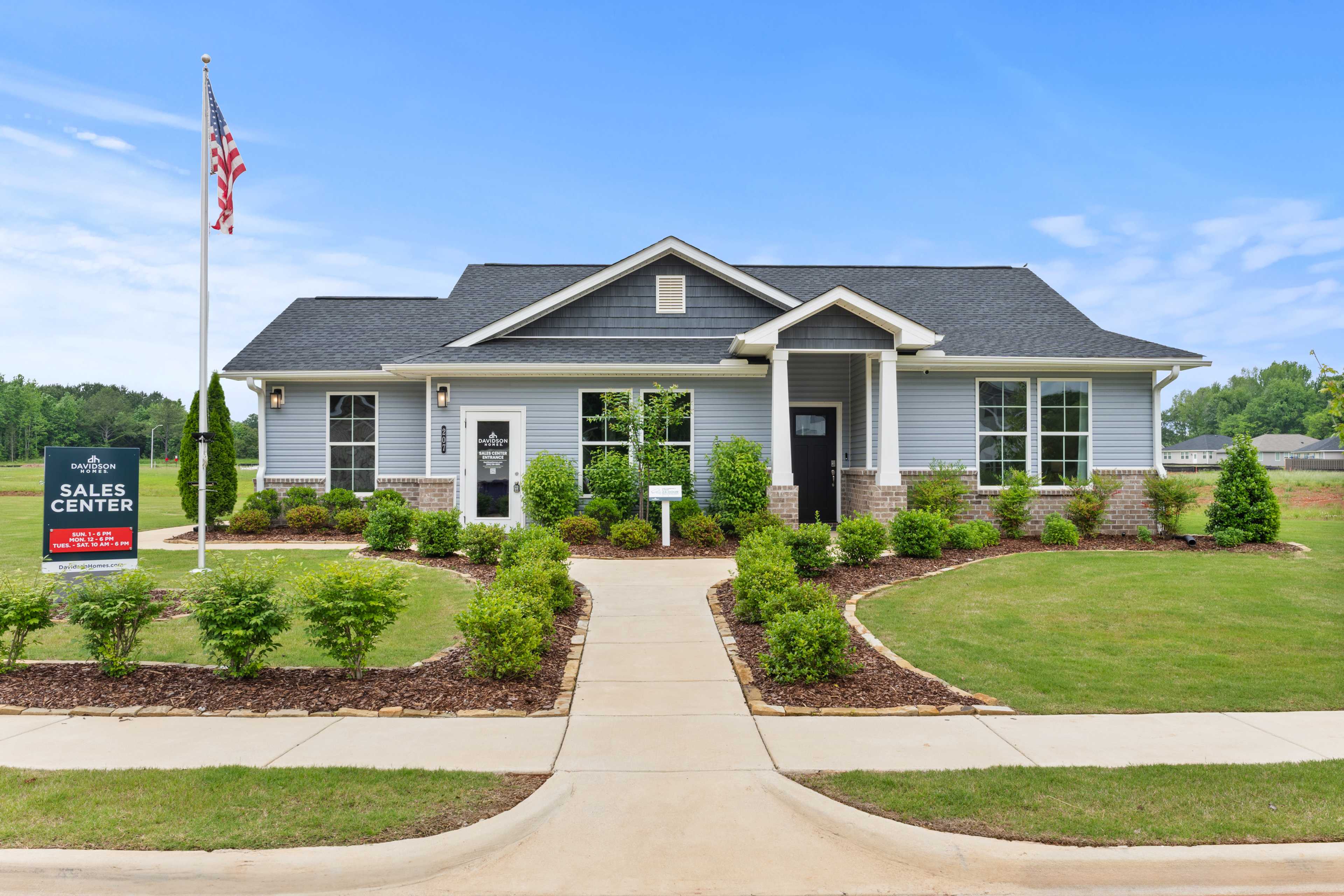 Sales center exterior at Forest Glen in Hazel Green Alabama by Davidson Homes featuring blue siding gabled roof and landscaped walkway
