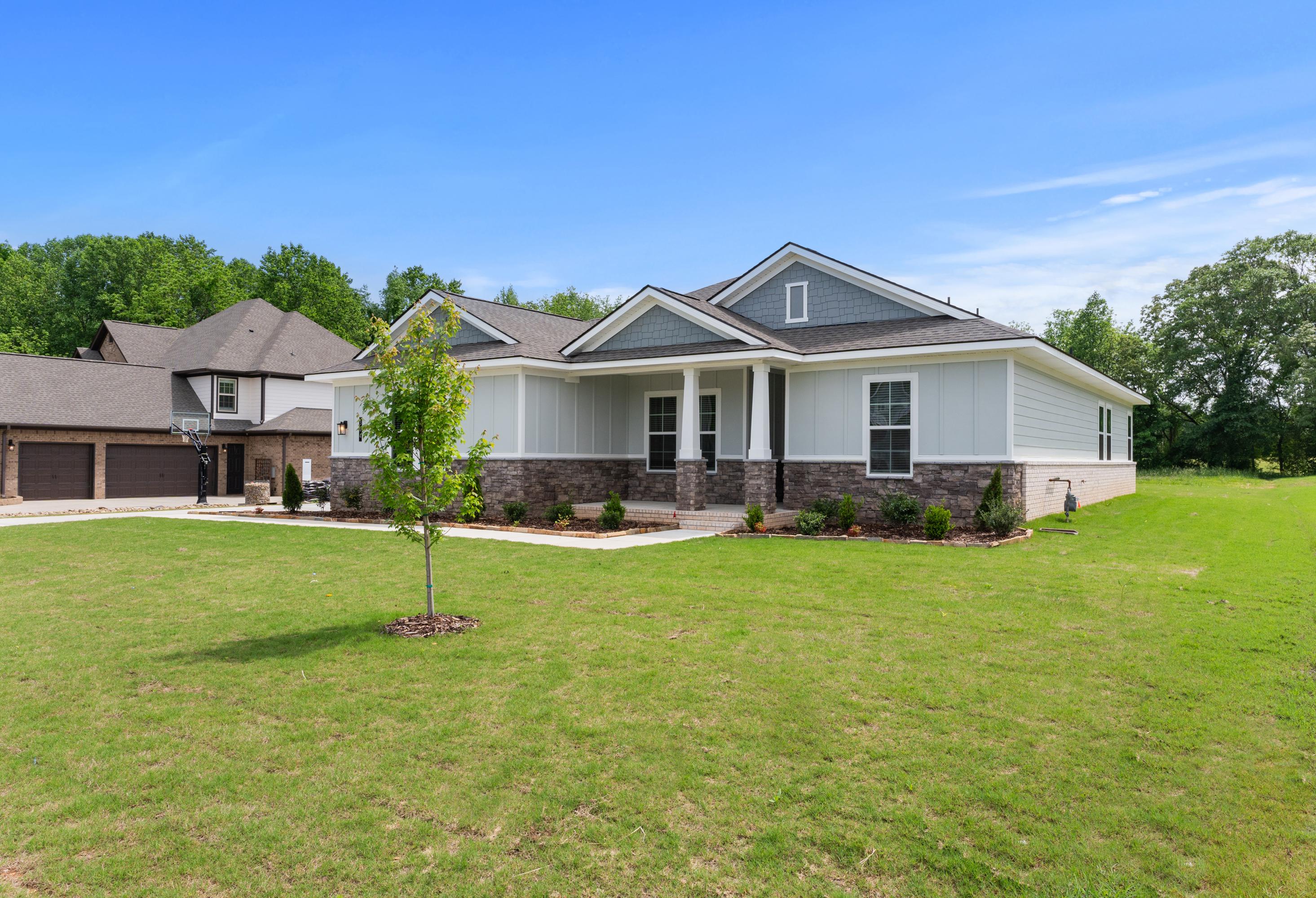 Modern single-story Arcadia B home elevation with gray siding, stone accents, covered porch, 3-car garage, and lush green lawn in Owens Cross Roads