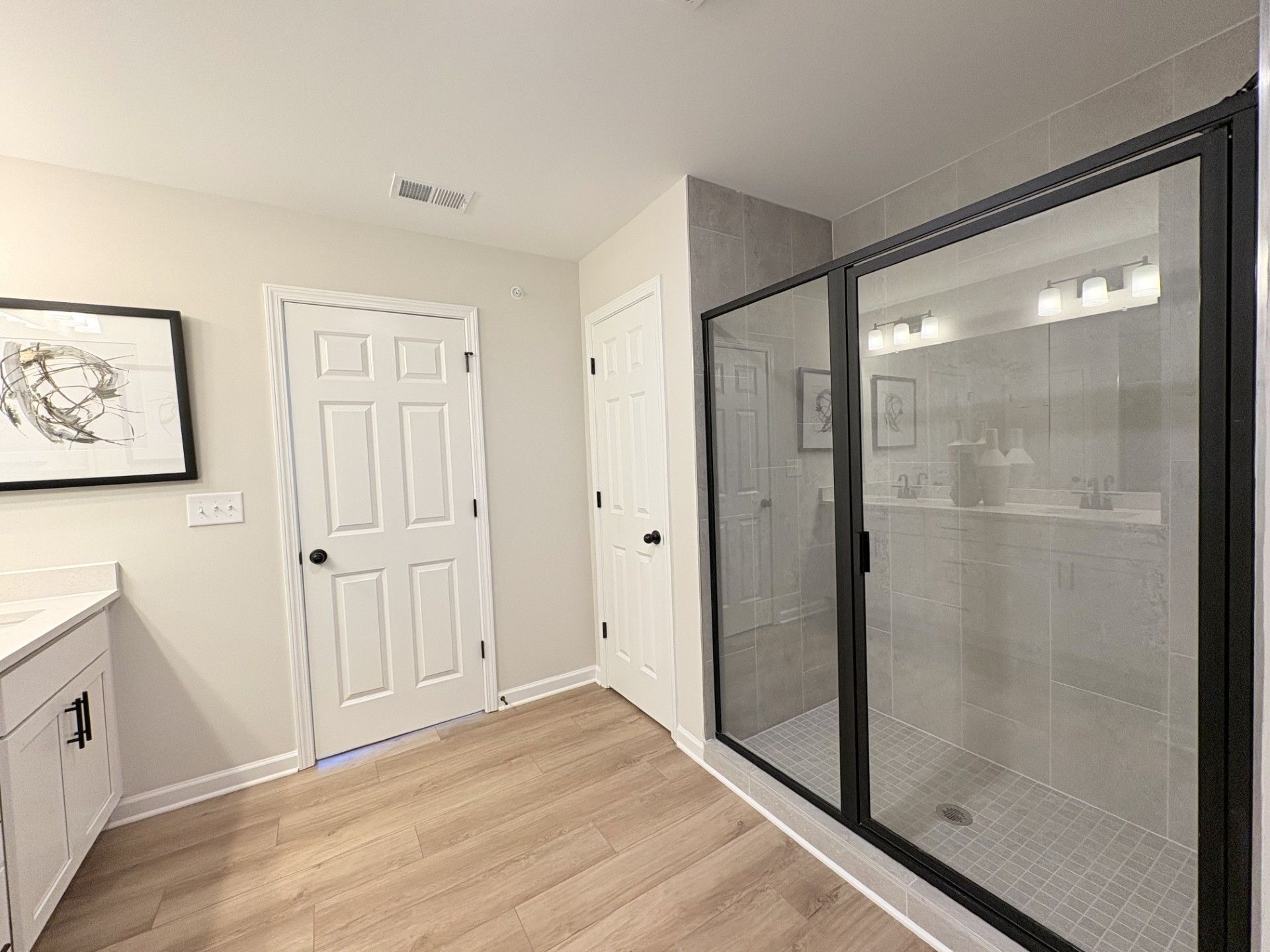 Modern primary bathroom in Hemingway Cumming GA with frameless glass shower, white vanity, hardwood floors