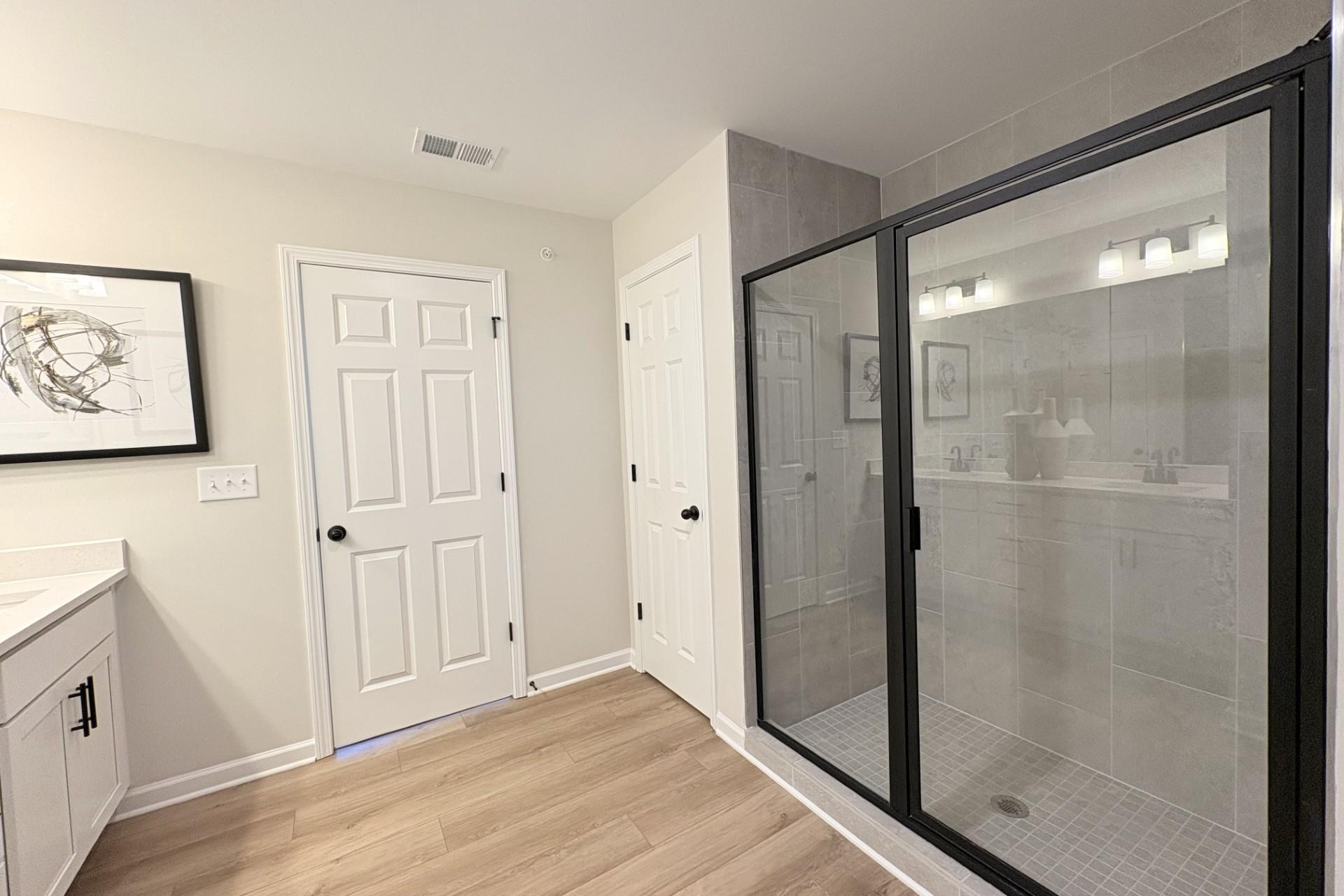Modern primary bathroom in Hemingway Cumming GA with frameless glass shower, white vanity, hardwood floors