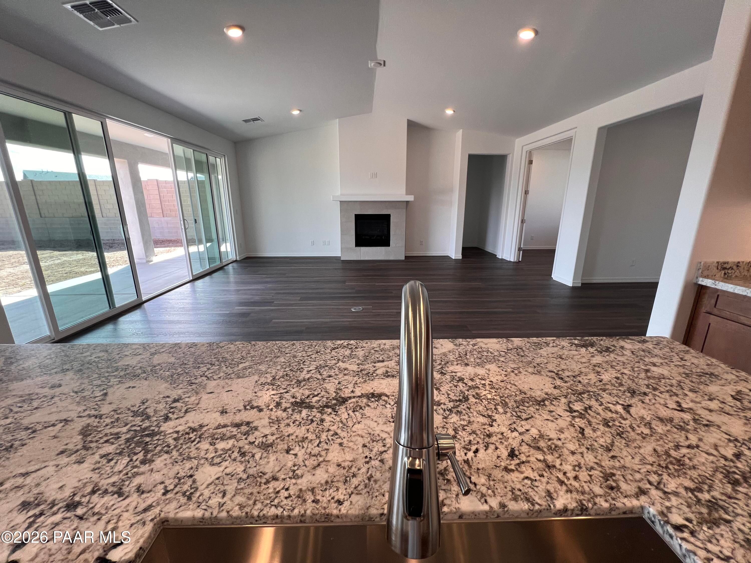 Open-concept kitchen with granite island and stainless faucet overlooking living room fireplace and backyard view in Davidson Homes The Monarch A, Prescott, AZ