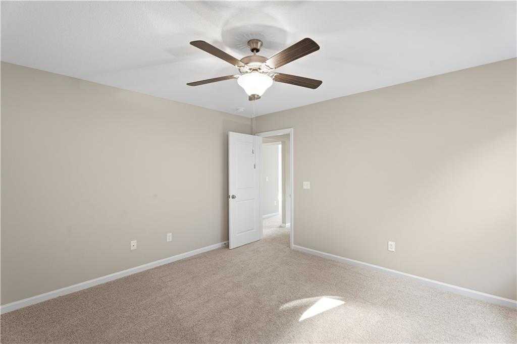 Spacious empty bedroom with ceiling fan, beige walls, carpet, and open door in Davidson Homes The Washington, Phenix City, Alabama