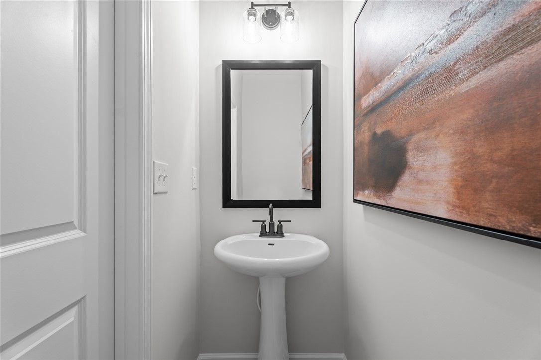 Stylish powder room with pedestal sink, black-framed mirror, and abstract wall art in Davidson Homes The Stella B, Opelika, Alabama