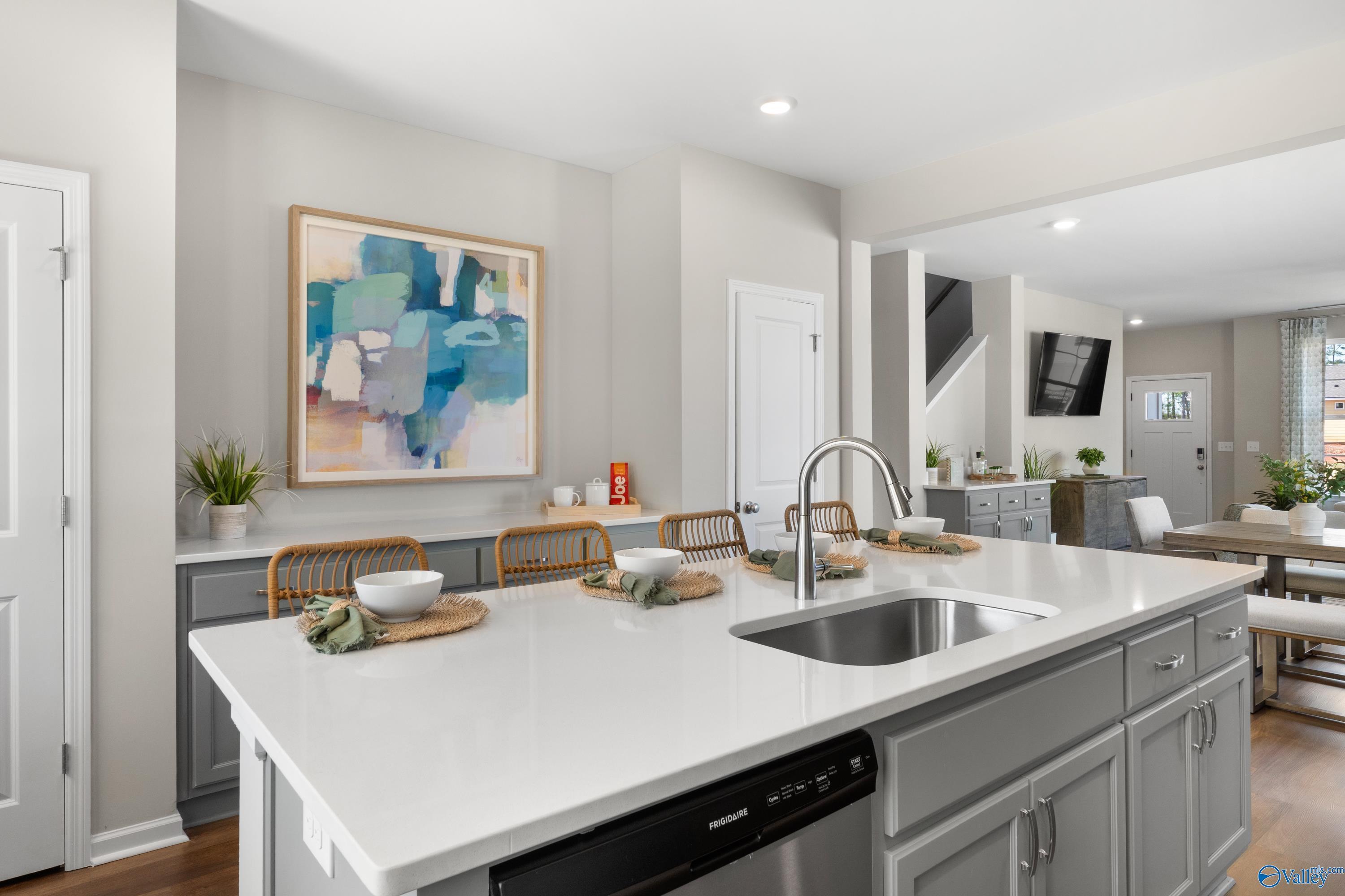 Modern kitchen island with white quartz counters, gray shaker cabinets, stainless sink, Frigidaire dishwasher in The Stella floor plan, Madison AL