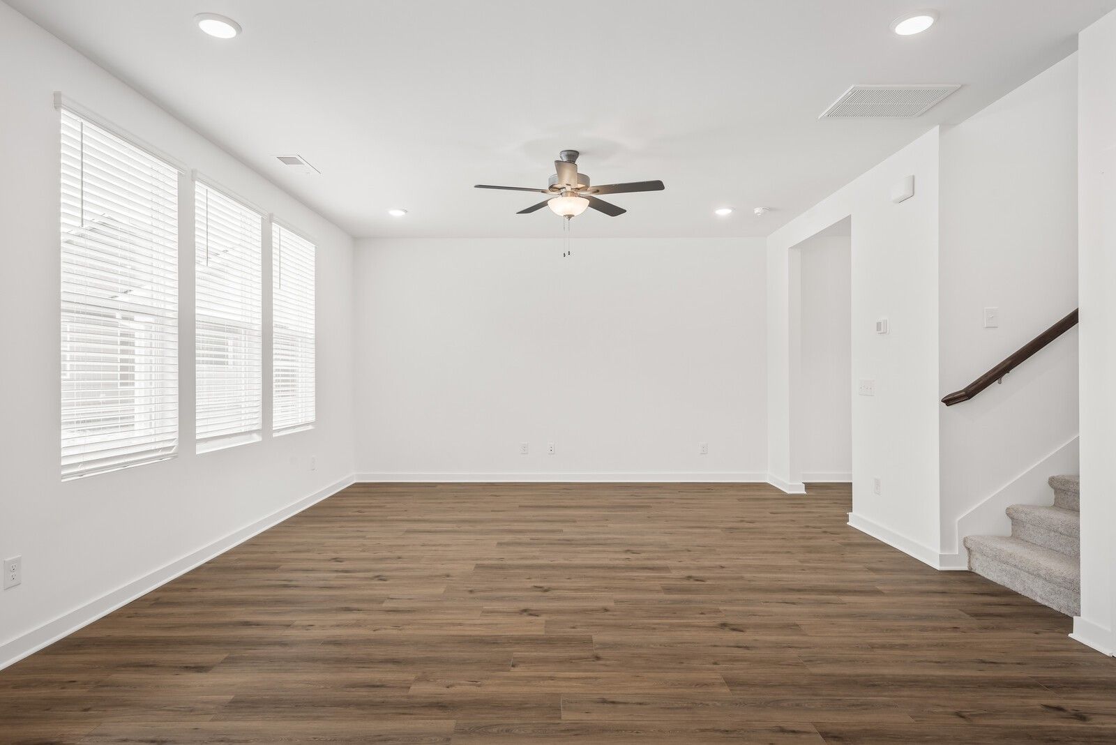 Bright empty living room with large windows, ceiling fan, hardwood floors, and staircase in Davidson Homes The Gordon C, White House, TN