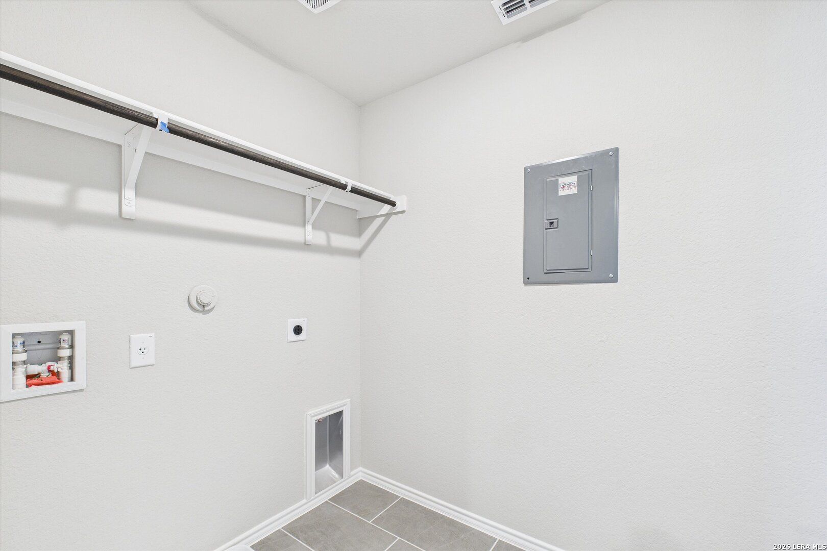 Bright laundry room with hanging rod, water heater, electrical panel, and pet door in Davidson Homes Charlotte A, San Antonio, Texas