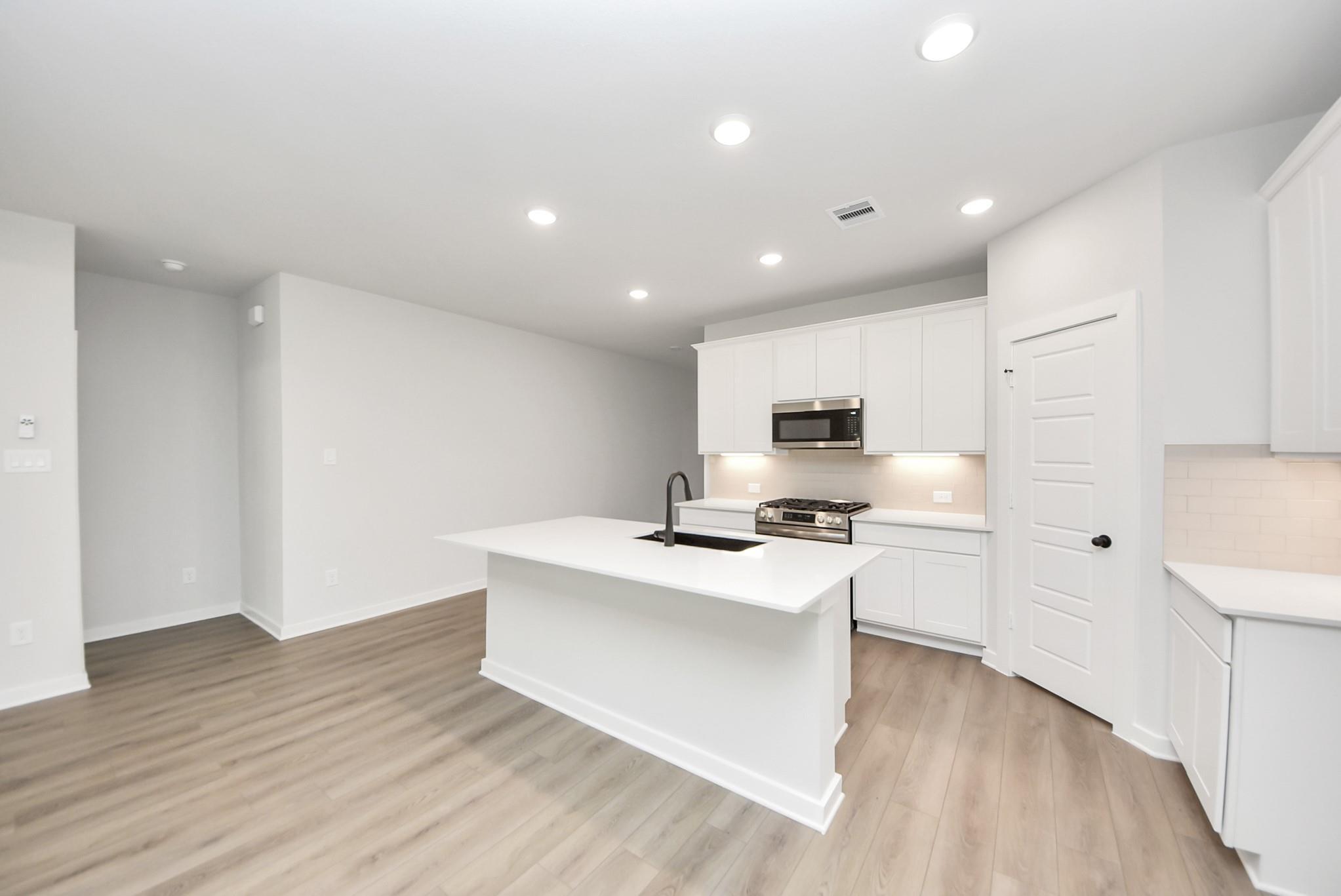Modern white kitchen with island, stainless appliances, and wood flooring in The Daphne F floor plan at Sundance Cove.