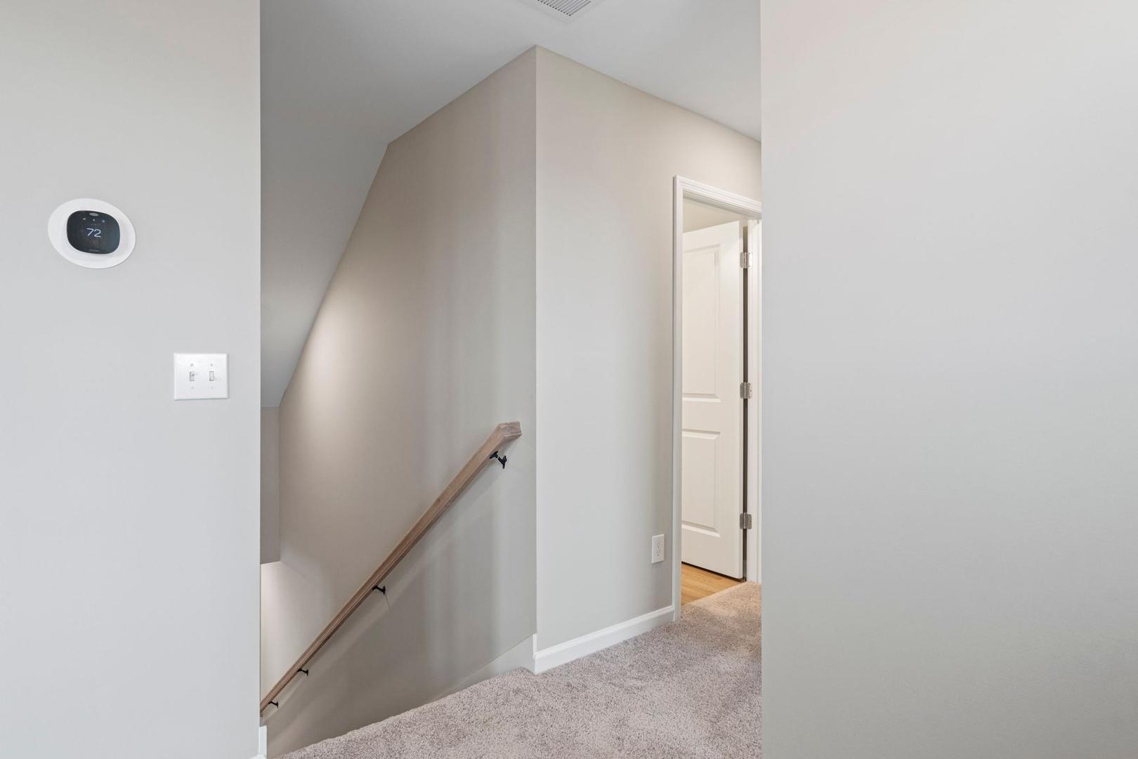 Upper-level hallway and staircase in The Stella A, 2-story home with beige walls, wooden handrail, open door, and neutral carpet