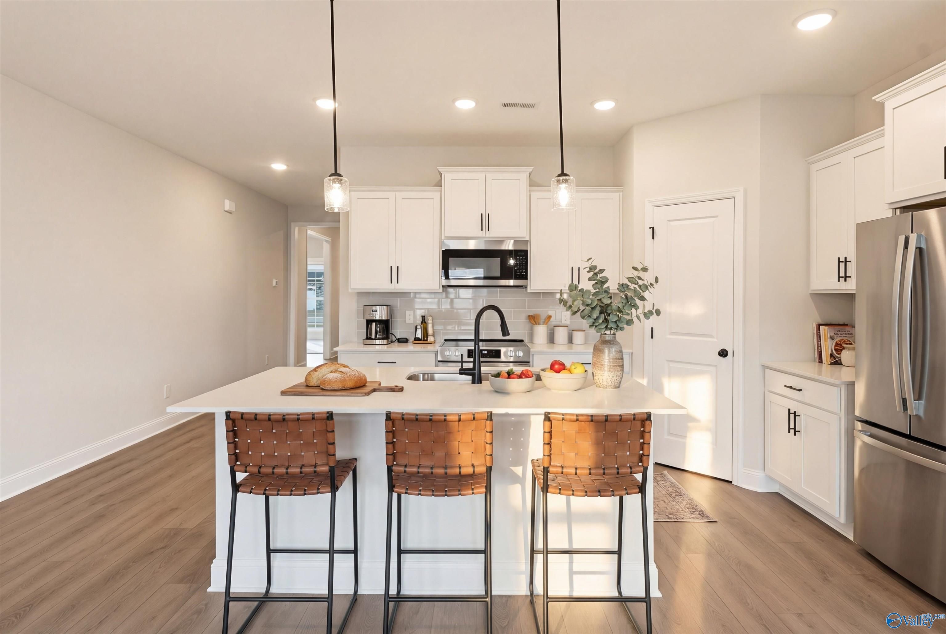 Modern white kitchen with island, leather bar stools, stainless appliances in The Daphne D by Davidson Homes, Arab, Alabama