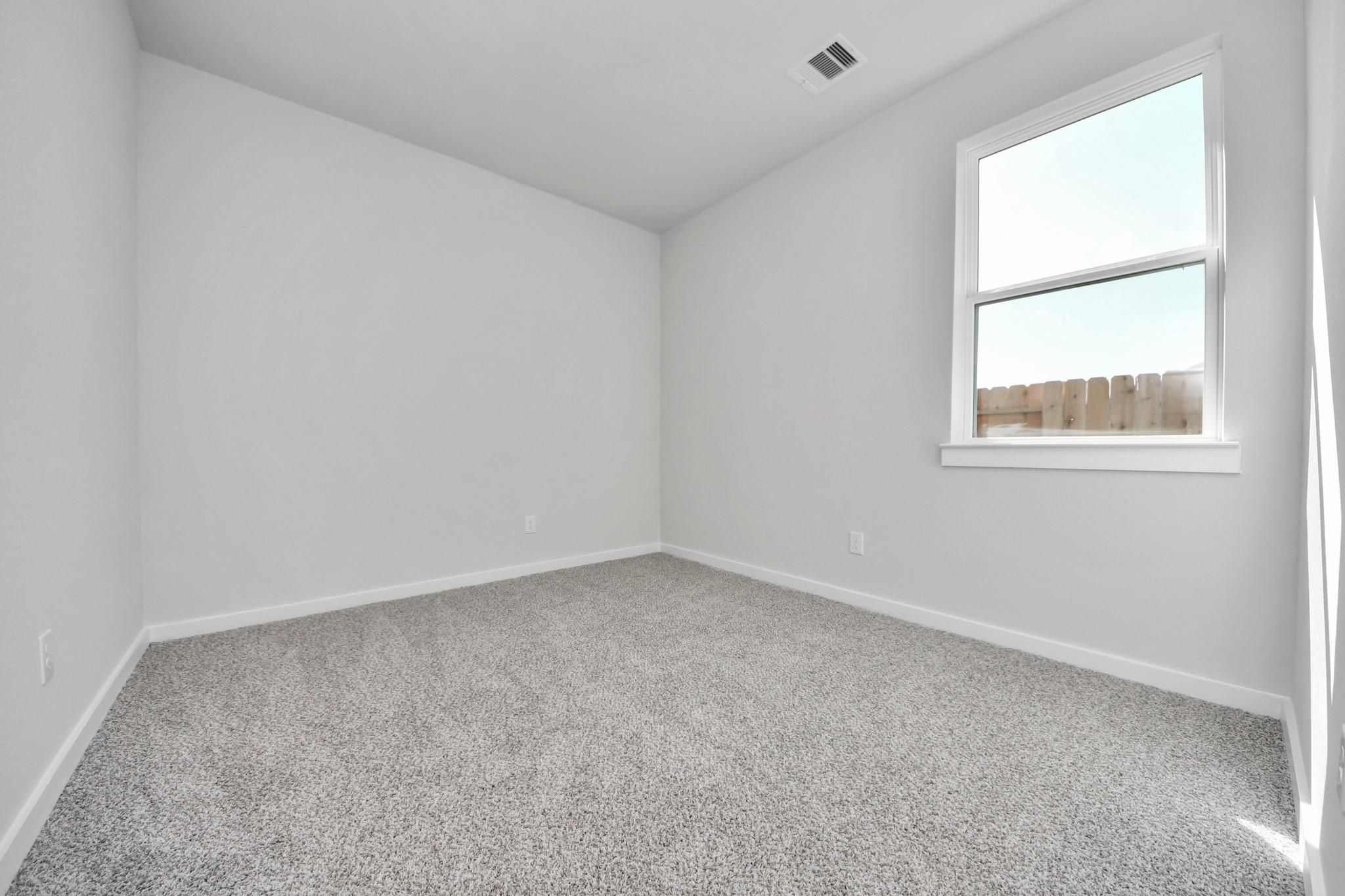 Bright, carpeted bedroom with neutral walls in The Colorado G floor plan at Emberly, Beasley, Texas.