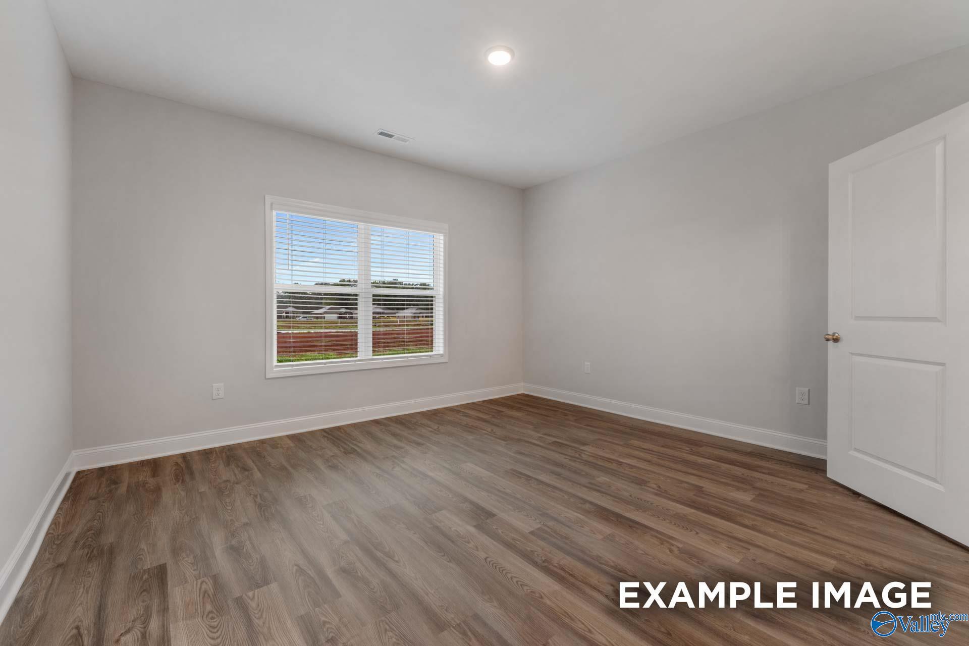 Bright secondary bedroom featuring large window with blinds and luxury vinyl plank flooring in Davidson Homes The Cumberland B, Decatur, Alabama