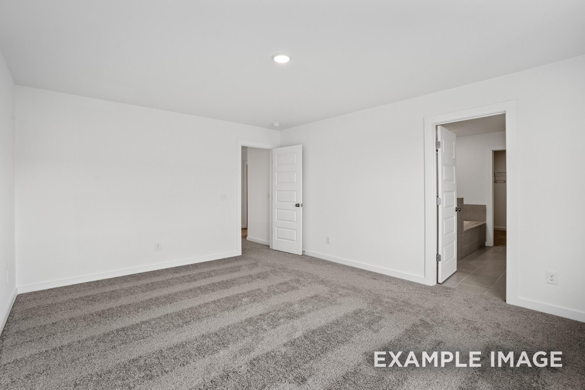 Spacious master bedroom in The Logan C featuring white walls, striped beige carpet, recessed lighting, and adjacent bathroom door