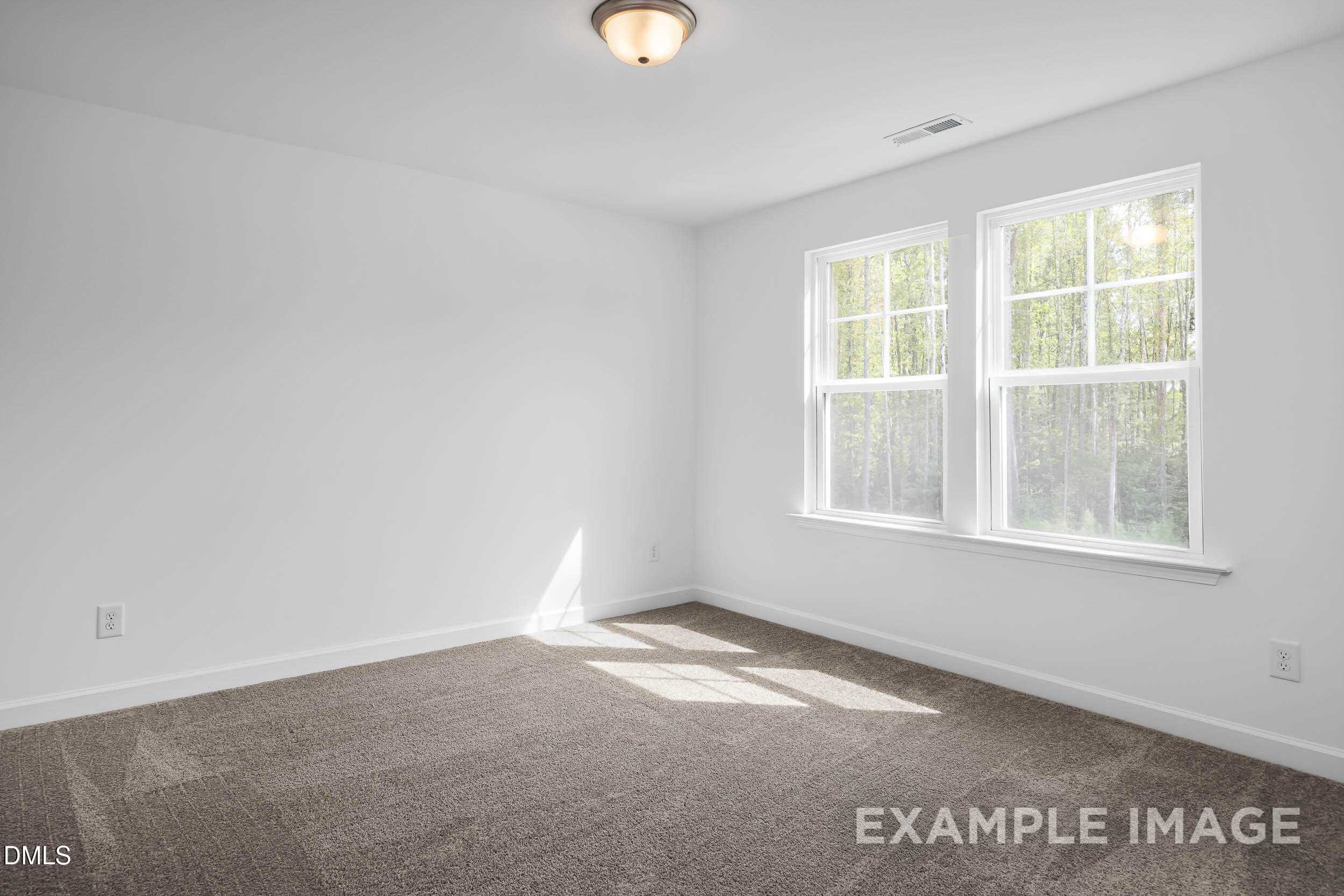 Bright empty bedroom with large windows overlooking trees, beige carpet in The Willow D 4-bedroom home, Zebulon, NC