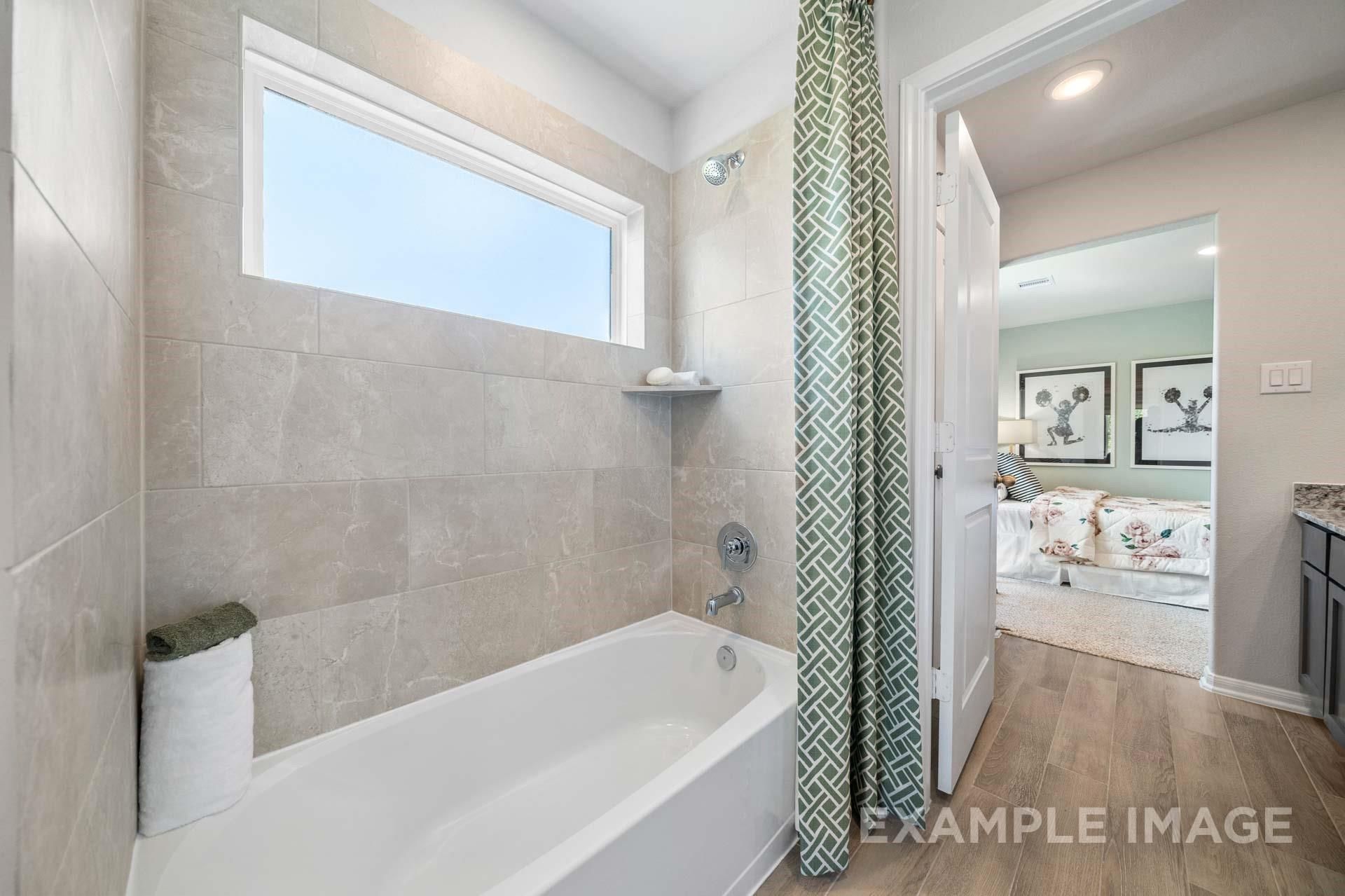 Elegant guest bathroom with soaking tub, green shower curtain, tiled walls, and bedroom view in 4-bed Davidson Homes Acadia A, Lago Mar, Texas City