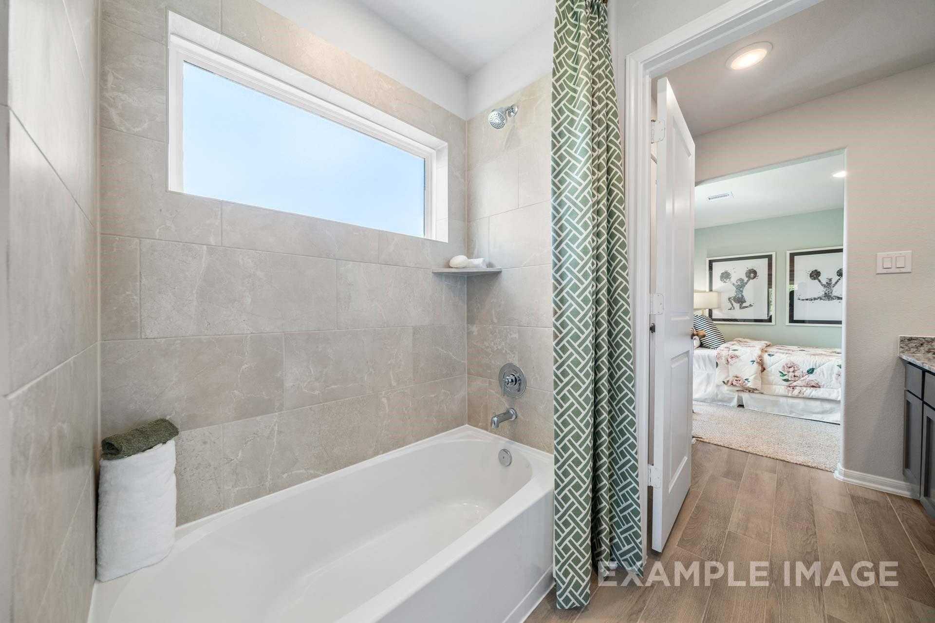 Elegant guest bathroom with soaking tub, green shower curtain, tiled walls, and bedroom view in 4-bed Davidson Homes Acadia A, Lago Mar, Texas City