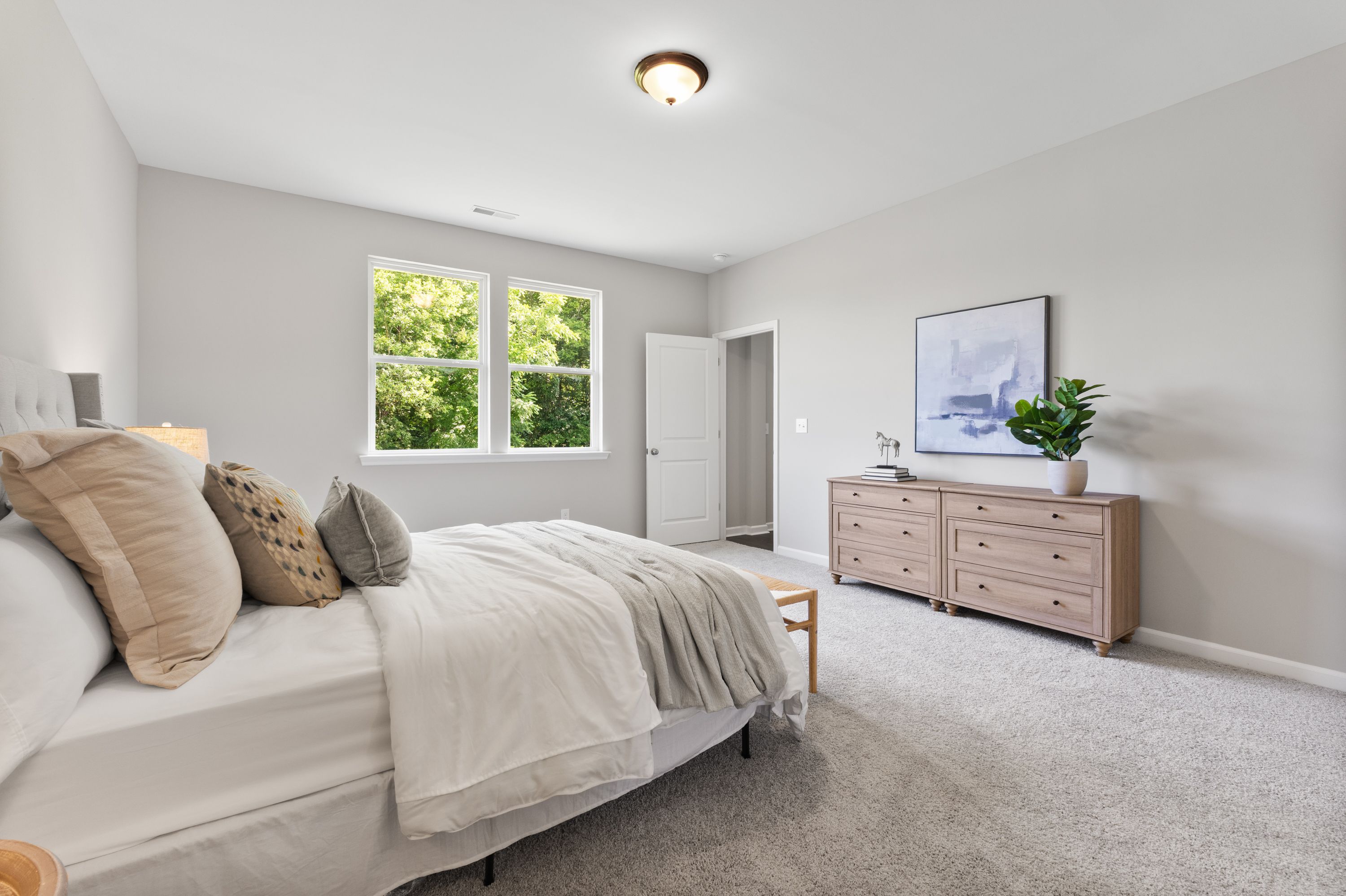 Spacious master bedroom in The Avalon E with king bed, oak dresser, and tree-view window
