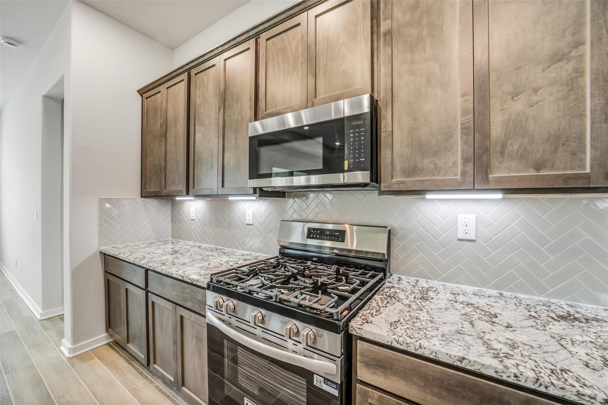 Modern kitchen with shaker cabinets, quartz countertops, stainless gas range and herringbone backsplash in The Acadia C, Magnolia TX