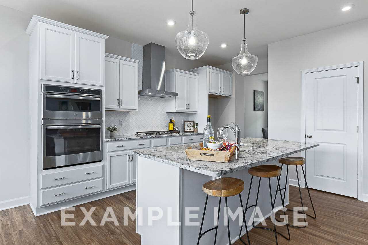 Modern kitchen in The Willow C featuring white shaker cabinets, granite island with bar stools, stainless steel double oven, and subway tile backsplash