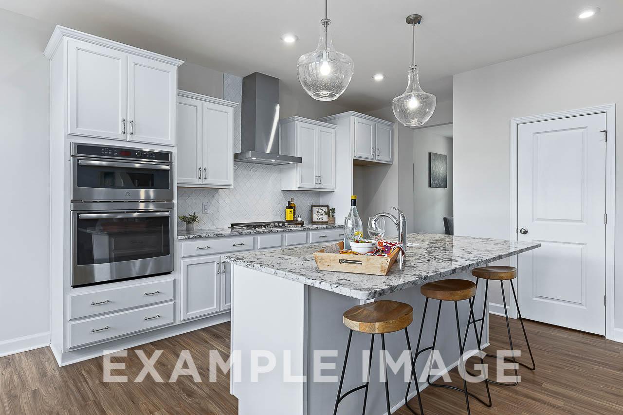 Modern kitchen in The Willow C featuring white shaker cabinets, granite island with bar stools, stainless steel double oven, and subway tile backsplash
