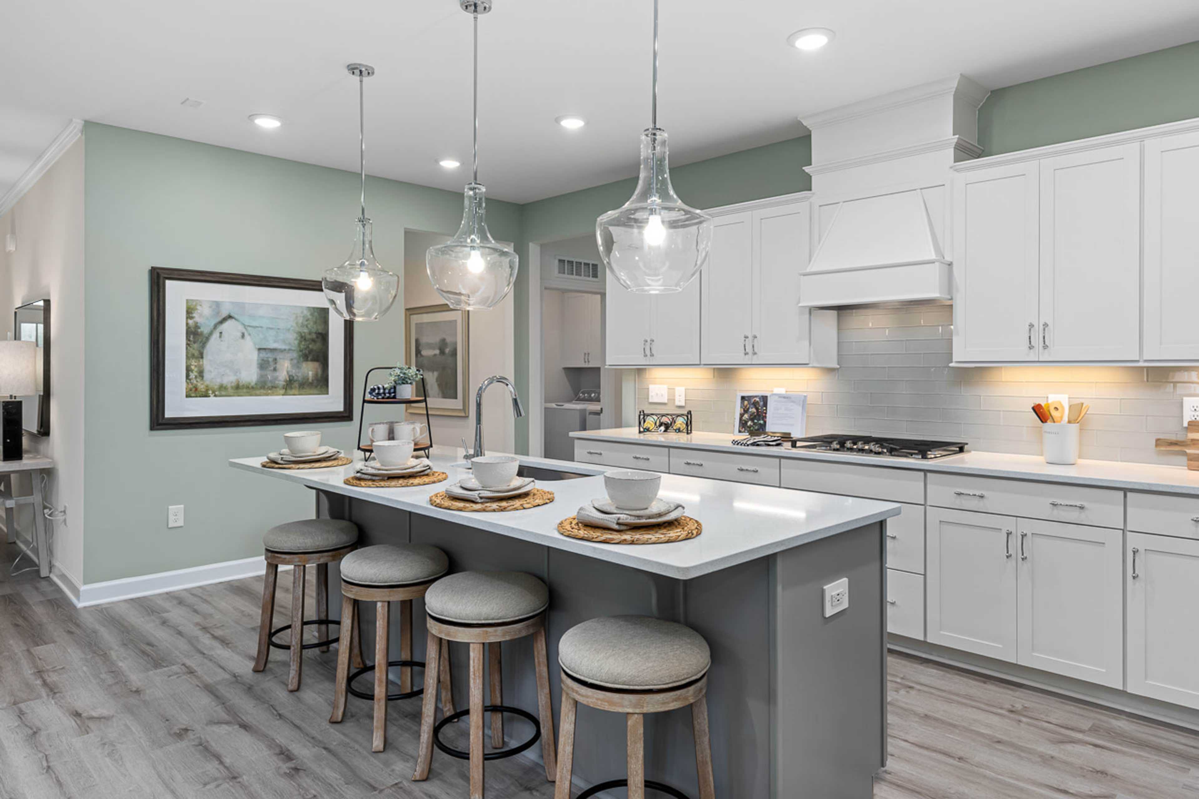 Spacious modern kitchen at Weatherford East in Angier NC with white shaker cabinets, gray quartz island, pendant lights and hardwood floors