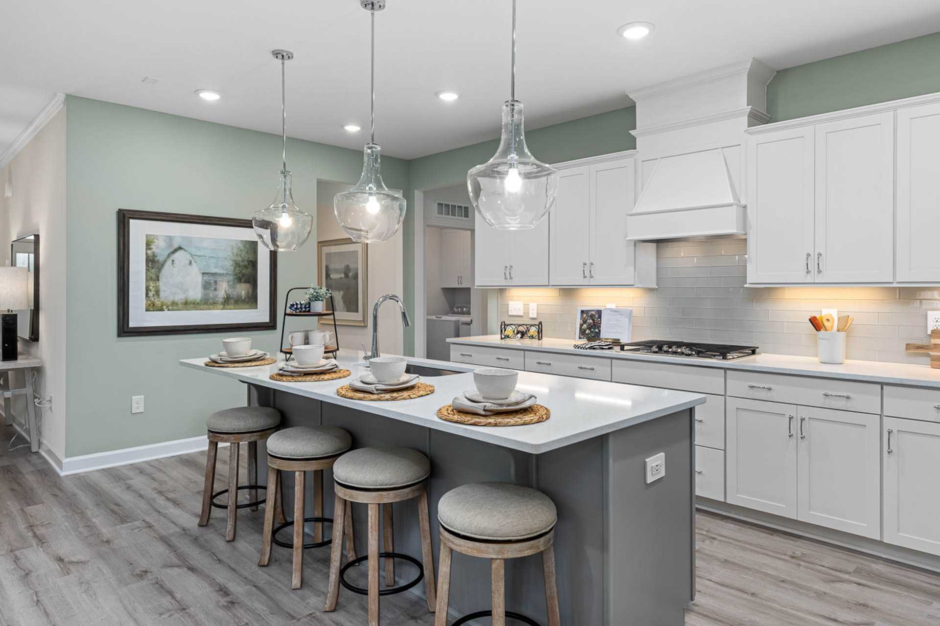 Spacious modern kitchen at Weatherford East in Angier NC with white shaker cabinets, gray quartz island, pendant lights and hardwood floors