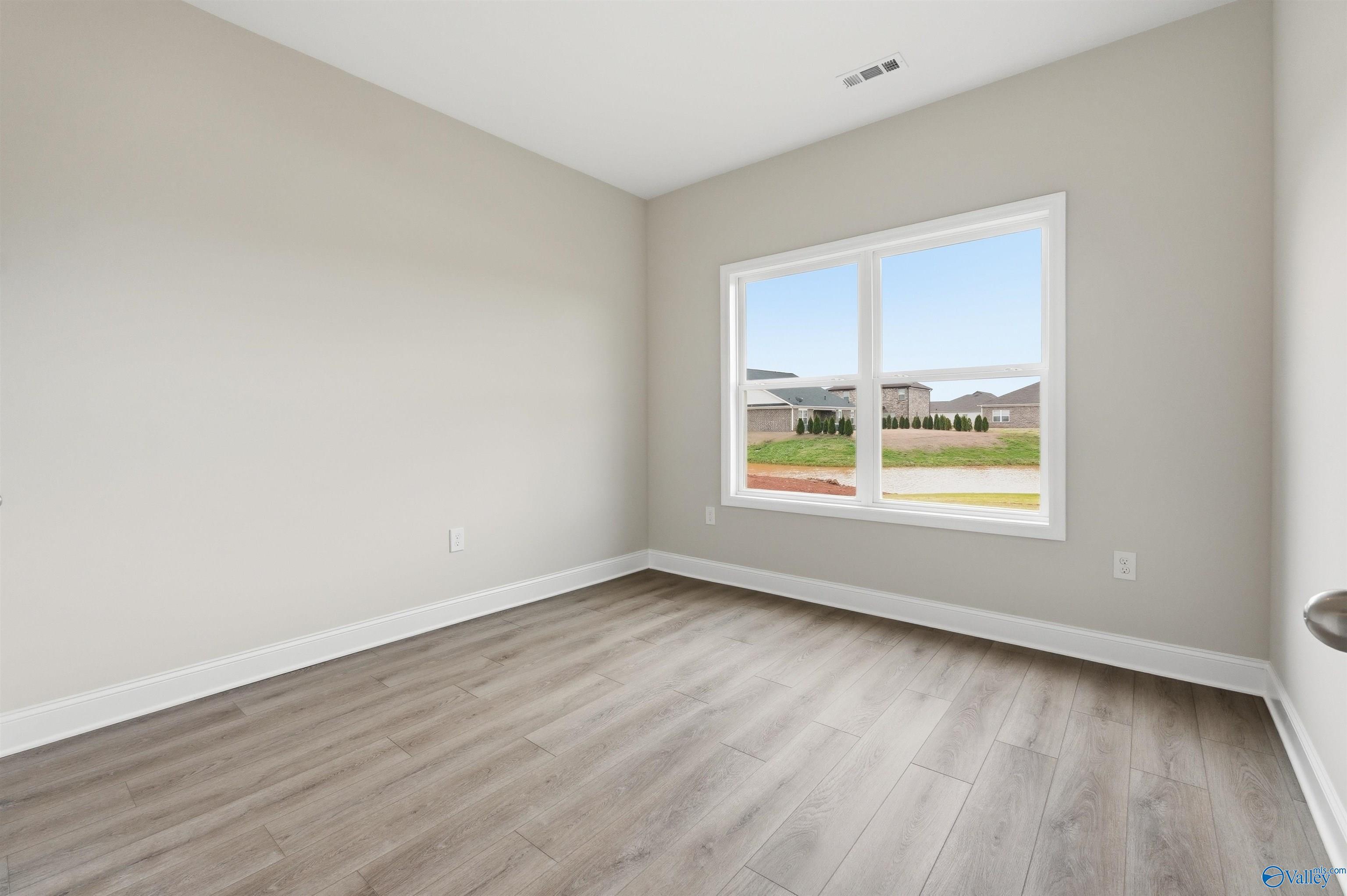 Unfurnished bedroom with wood-look flooring and large window in The Shelby D floor plan at Evergreen Mill, Madison, AL.