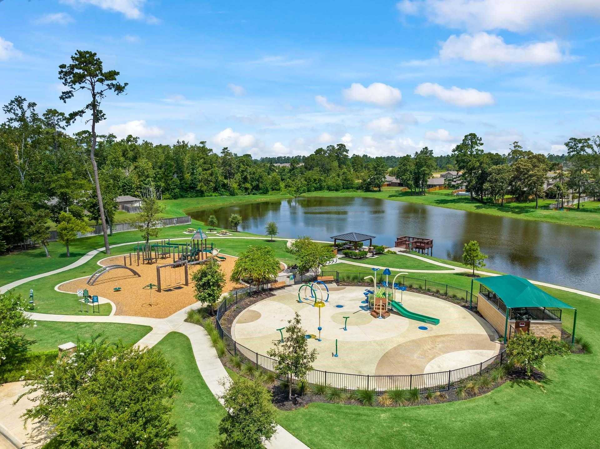 Vibrant playground with splash pad, slides, and swings beside serene lake in Lakes at Black Oak, Magnolia, Texas