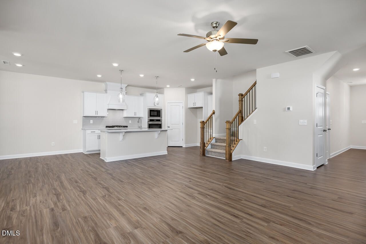 Open kitchen with white shaker cabinets, large island, and built-in oven near wooden staircase in The Grace C home by Davidson Homes, Lillington, NC