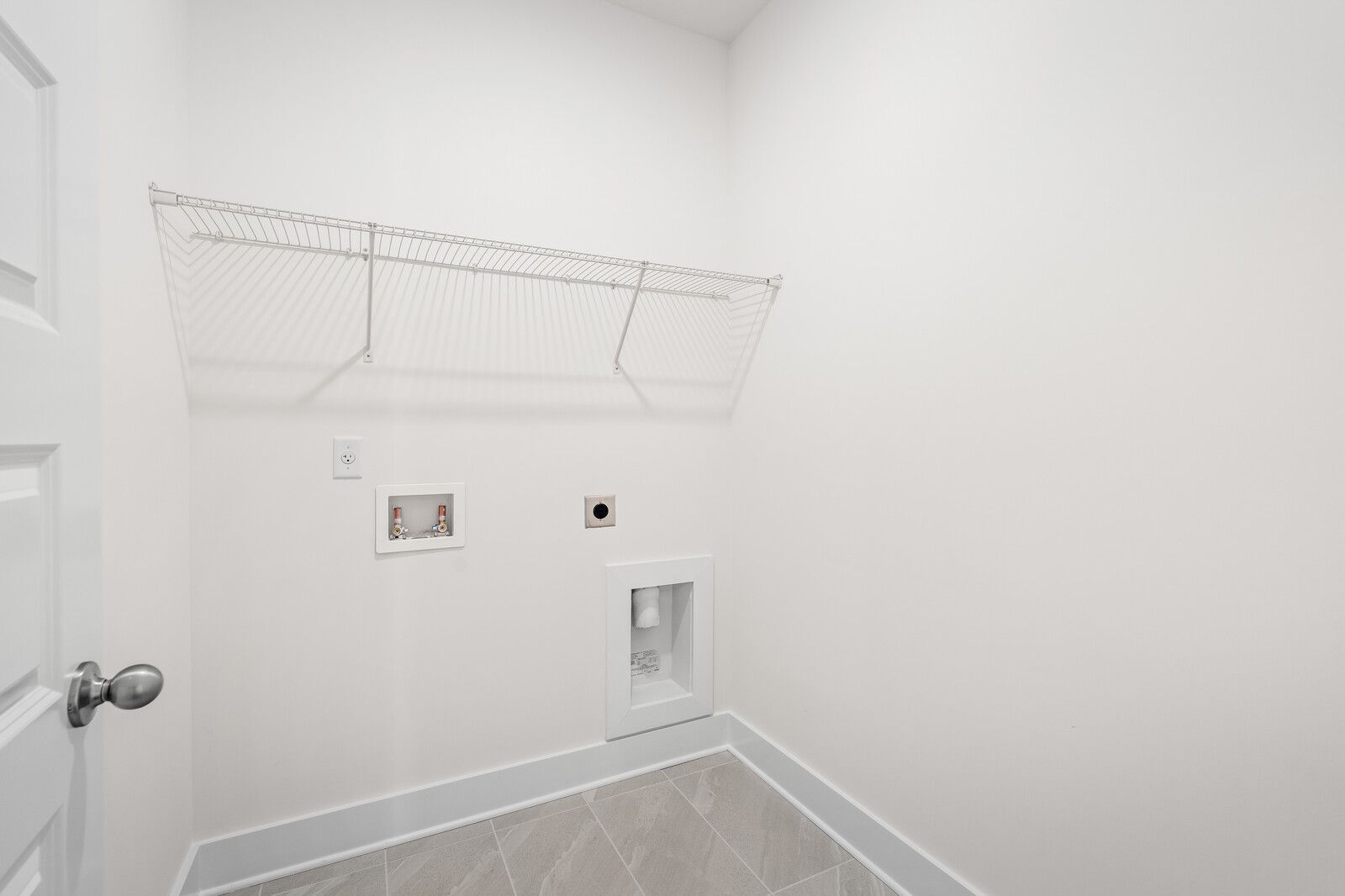 Bright laundry room in The Cottonwood floor plan featuring wall-mounted wire shelving and hookups for washer and dryer.