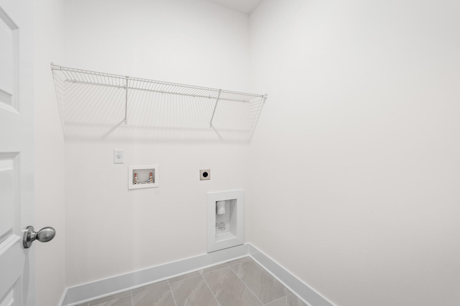 Bright laundry room in The Cottonwood floor plan featuring wall-mounted wire shelving and hookups for washer and dryer.
