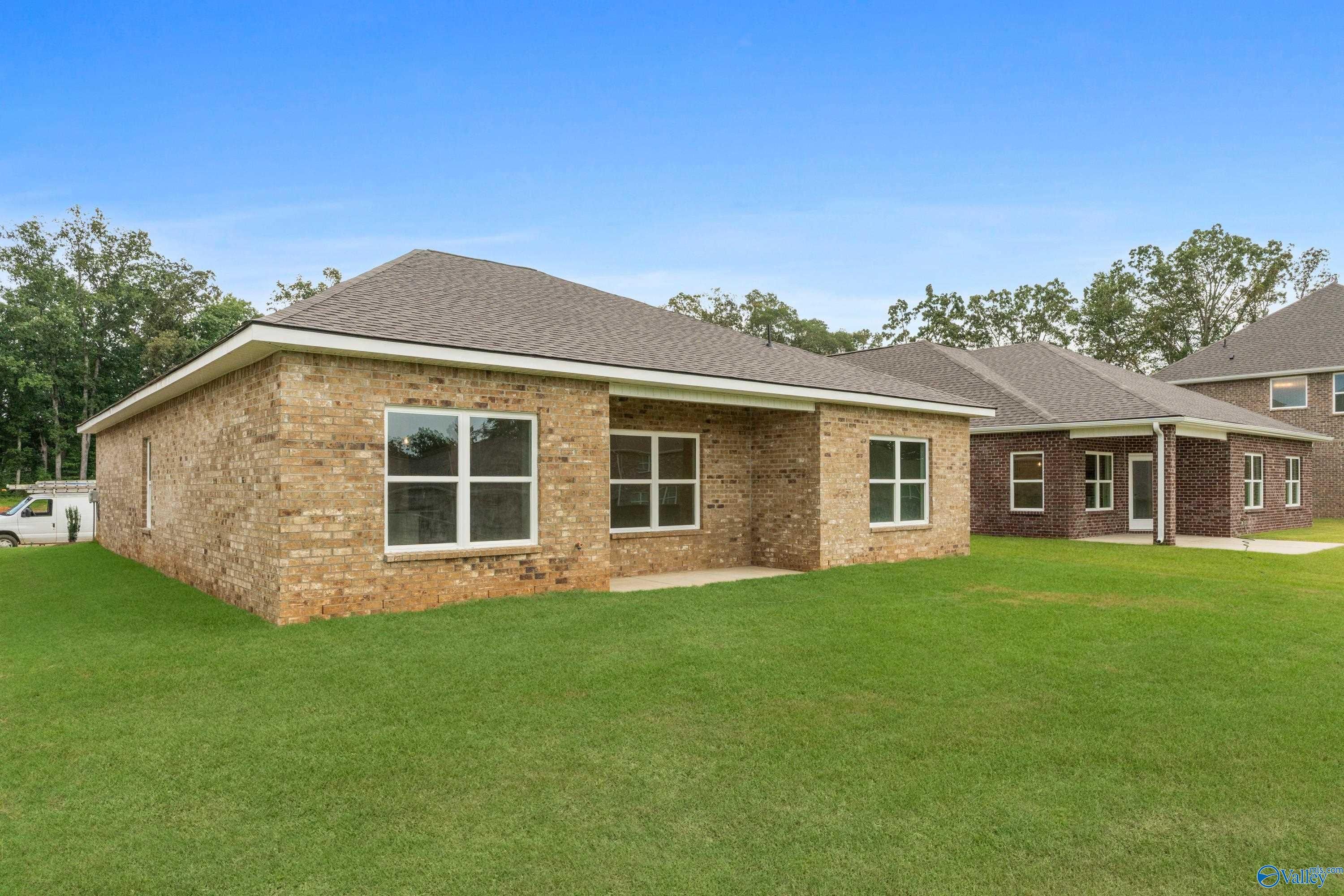 Single-story brick home with 2-car garage, large windows, lush green lawn, and trees in Creek Grove, New Market, Alabama