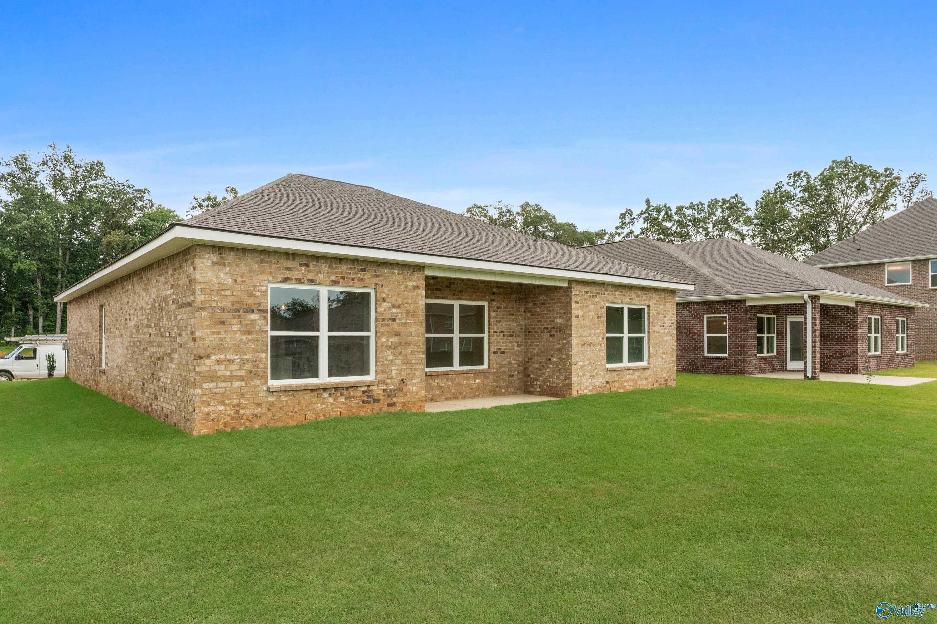 Single-story brick home with 2-car garage, large windows, lush green lawn, and trees in Creek Grove, New Market, Alabama
