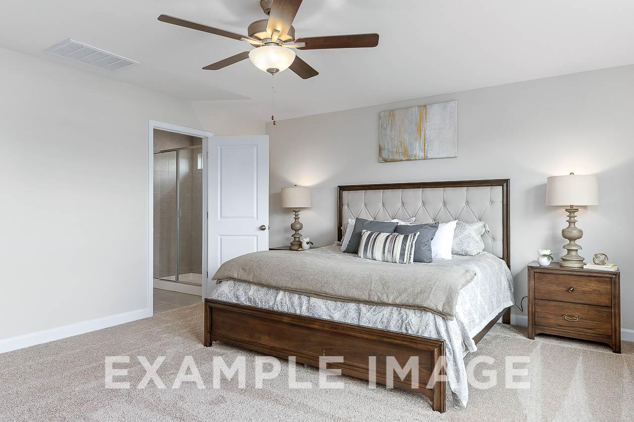 Spacious master bedroom in The Willow C featuring king bed with upholstered headboard, nightstands, lamps, ceiling fan, and en-suite bath access